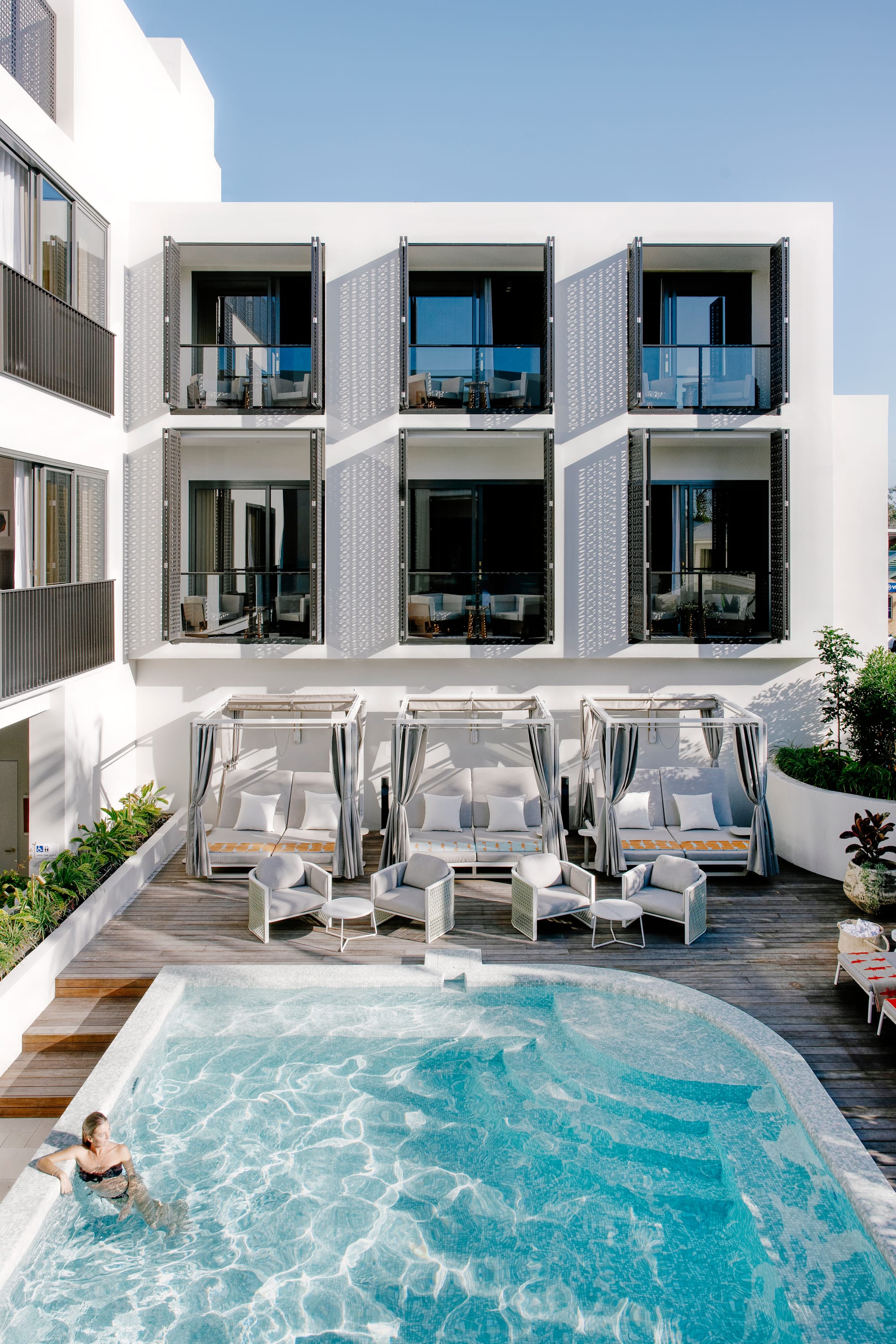 An exterior shot of the central pool showing a swimmer resting on the side and day beds and the white hotel in the background