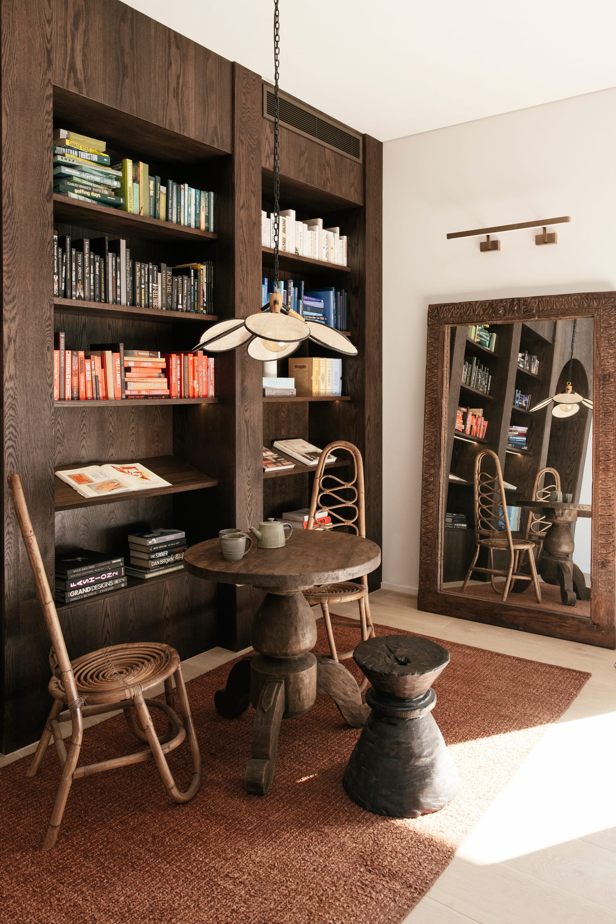 Basq House. Photography by Elise Hassey. Dark timber bookcase and table and chairs. Timber mirror and red rug.