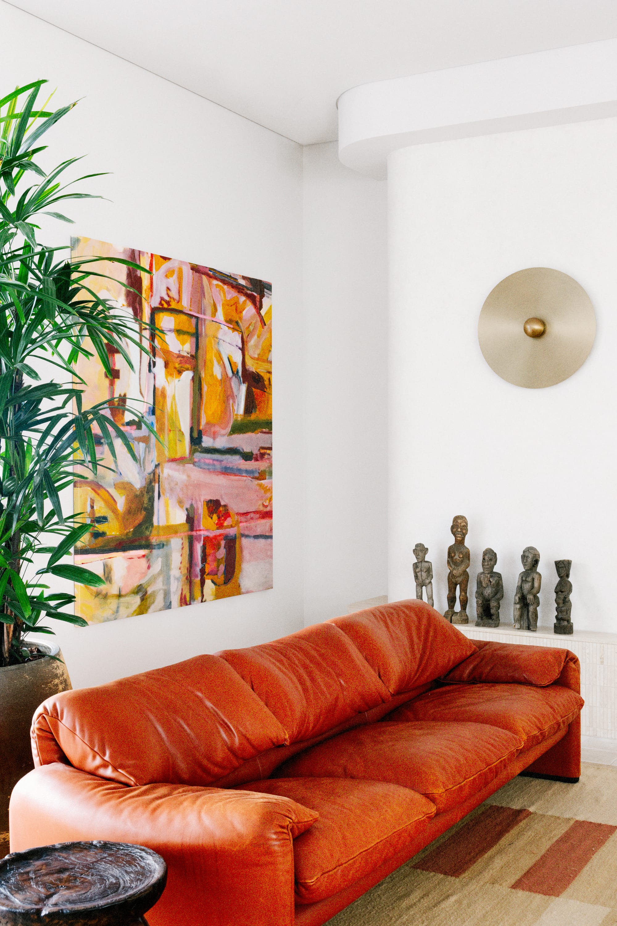 Basq House. Photography by Elise Hassey. Orange-red couch on patterned rug in front of abstract wall art and sculptures.