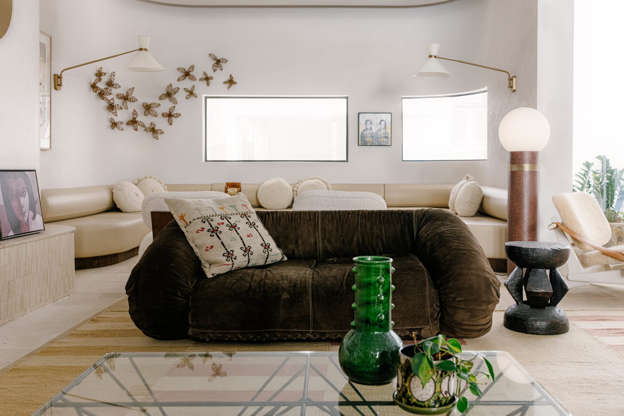 Basq House. Photography by Elise Hassey. Dark green-brown couch in front of integrated cream leather curved couch. Textured rugs and throw pillows.