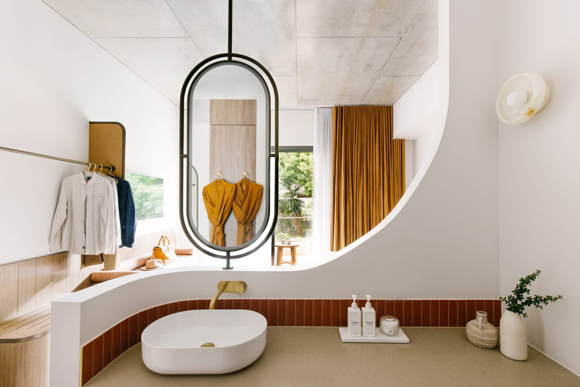 Basq House. Photography by Elise Hassey. Hotel room bathroom with curved half-wall and hanging curved mirror.