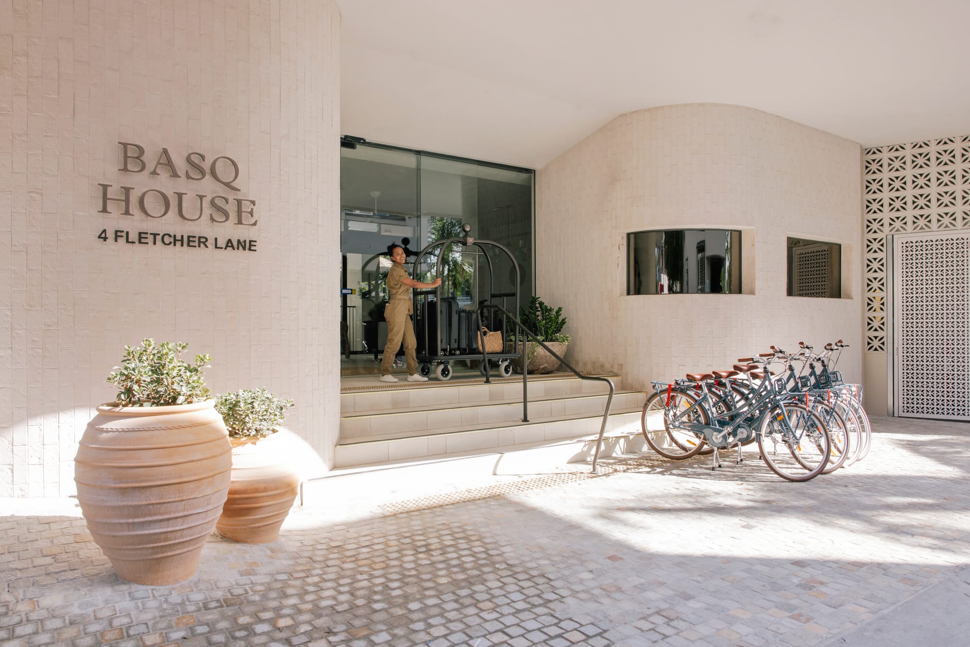 Basq House. Photography by Elise Hassey. Hotel entrance with stairs leading to front door and tiled walls. Bikes at front to right.