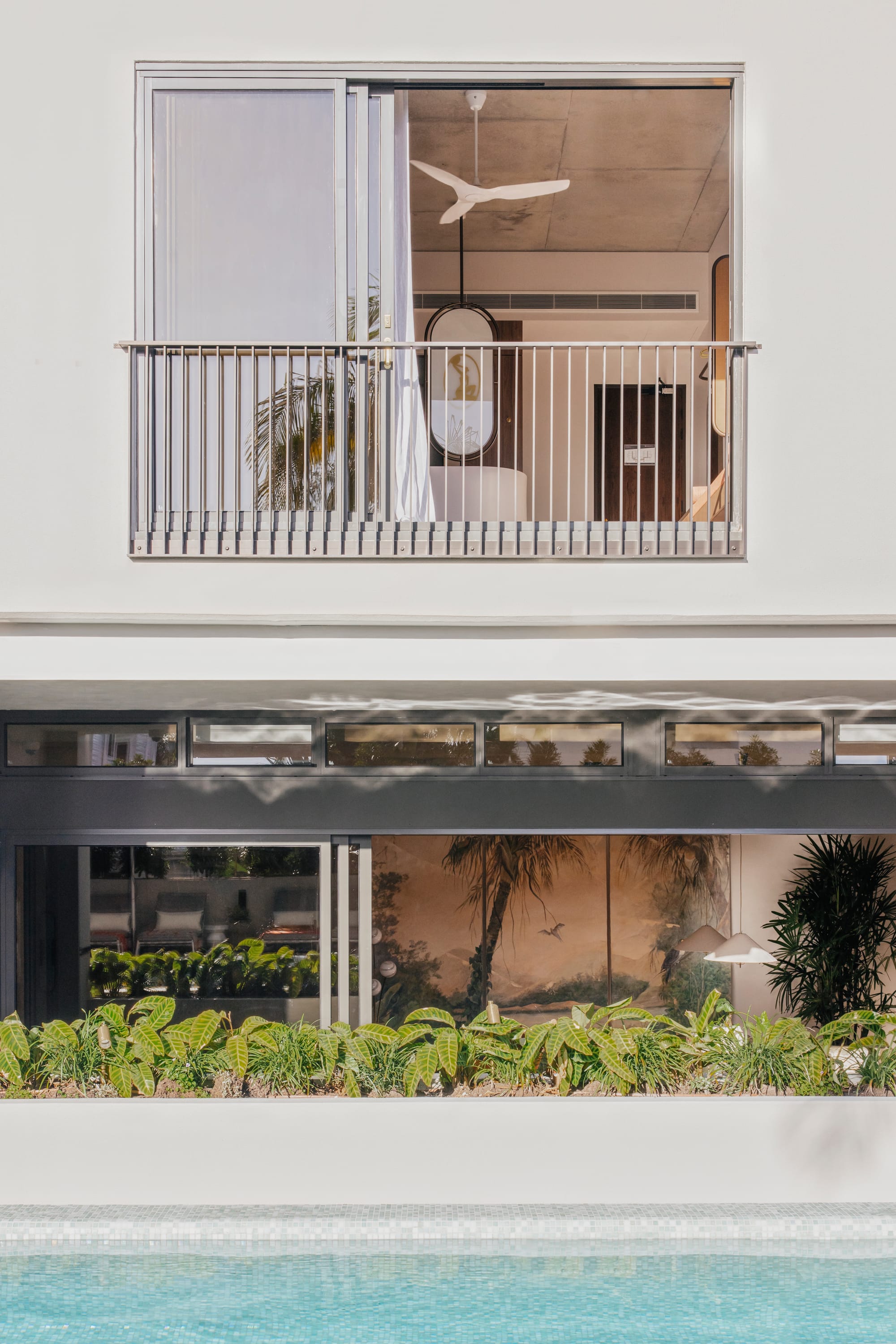 An exterior shot showing the hotel facade with the large sliding doors open to the communal areas and the pool in the foreground and a balcony above