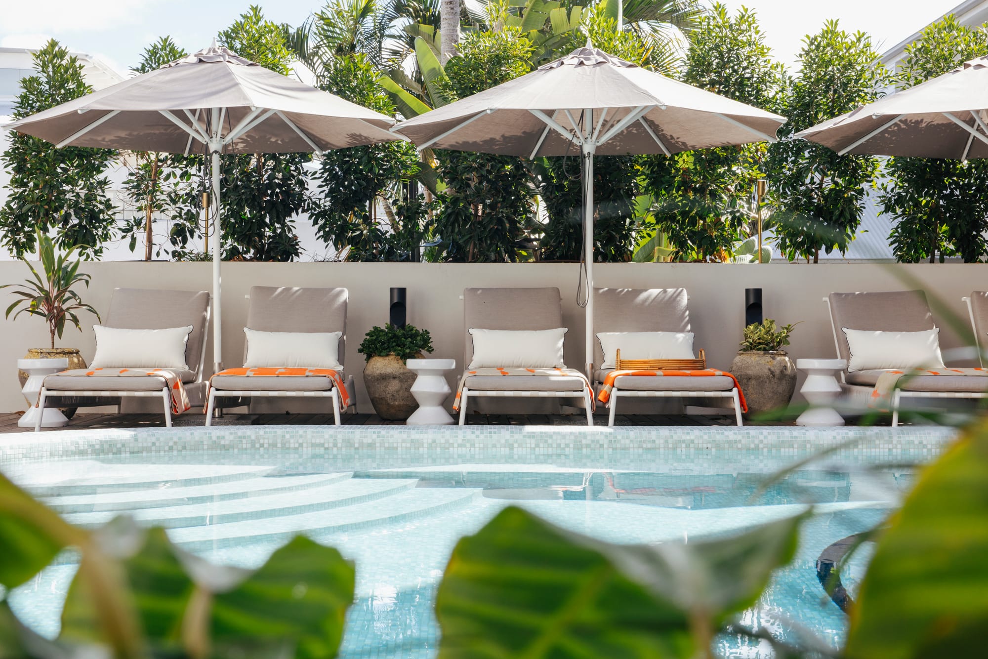 Basq House. Photography by Elise Hassey. Grey and white pool chair sunder grey umbrellas by tiled pool. 