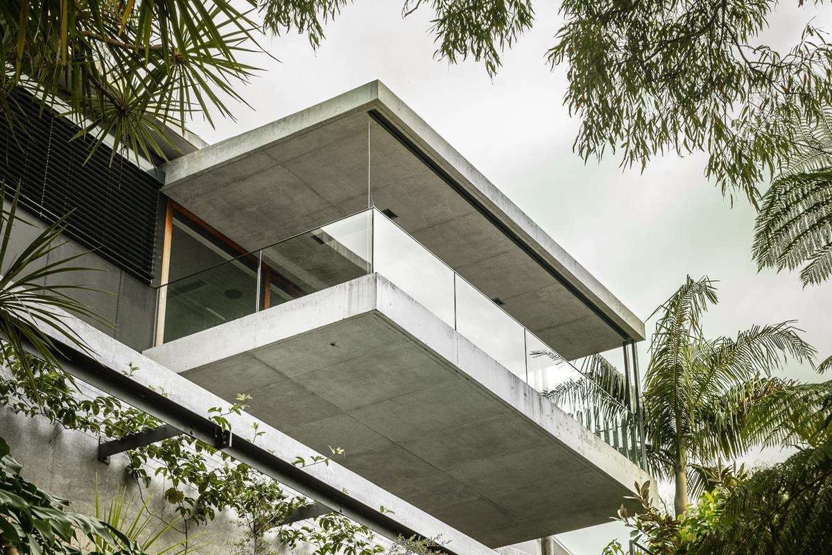 Bay House by Castlepeake Architecture. Photography by Felix Mooneeram. Low angle of concrete and glass balcony overhand on modern residential build surrounded by tropical plants. 