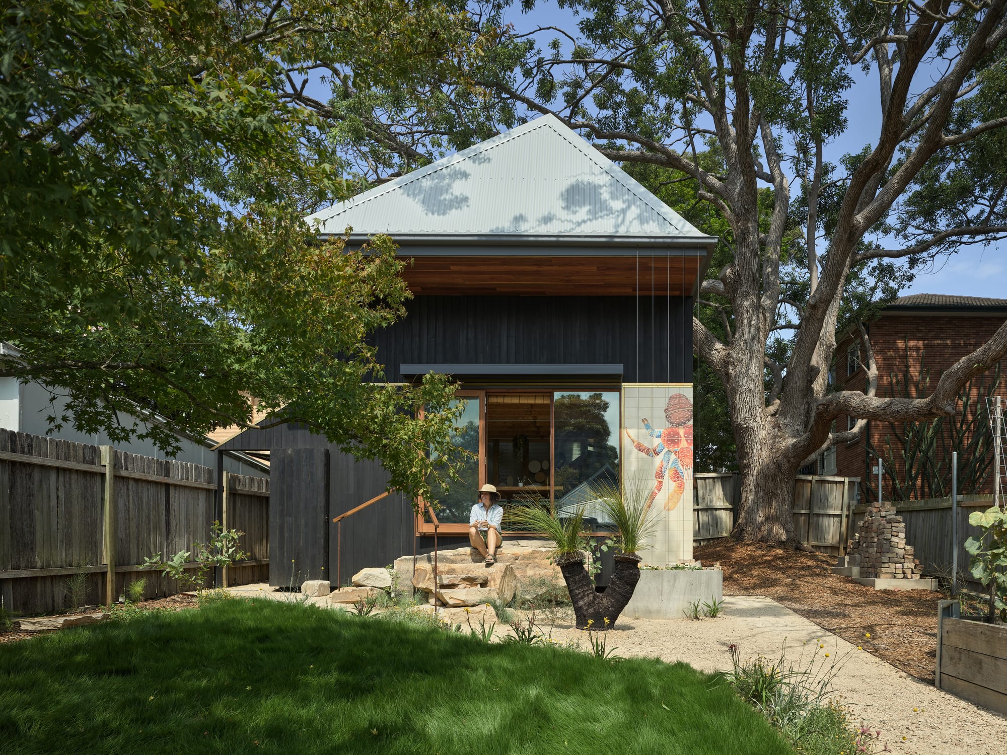 Coconut Crab by Alexander Symes Architect. Photography by Barton Taylor Photography. Outdoor studio with dark timber clad exterior and square tin roof. Surrounded by long green grass and vegetable patch.