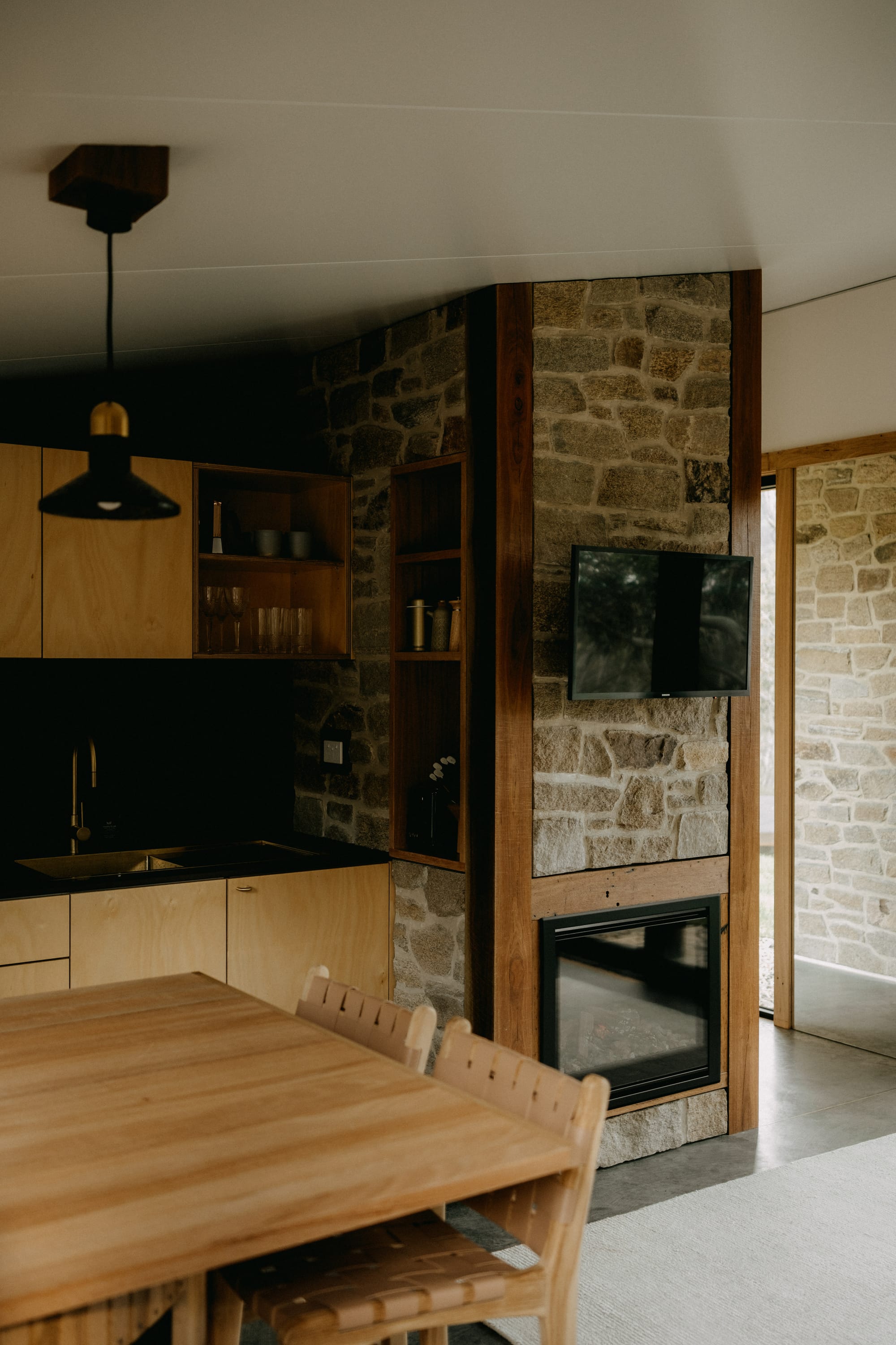 Crafters Eco-Cabins. Image copyright of Crafters. Stone walls in interior kitchen, with raw plywood veneer cabinetry and black splashback.