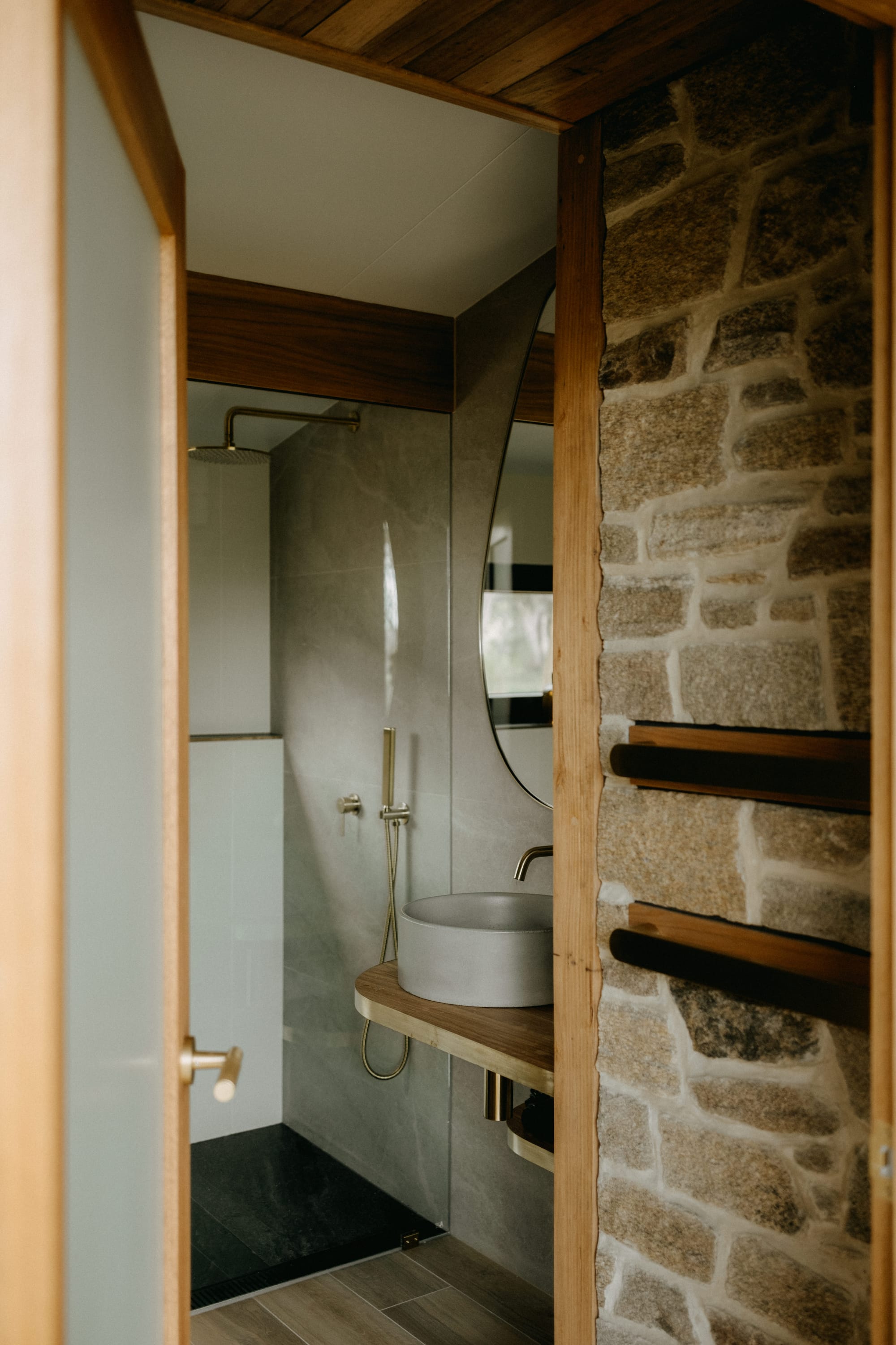 Crafters Eco-Cabins. Image copyright of Crafters. Stonework wall with timber framed frosted glass door opening onto bathroom with concrete wall and timber floors.