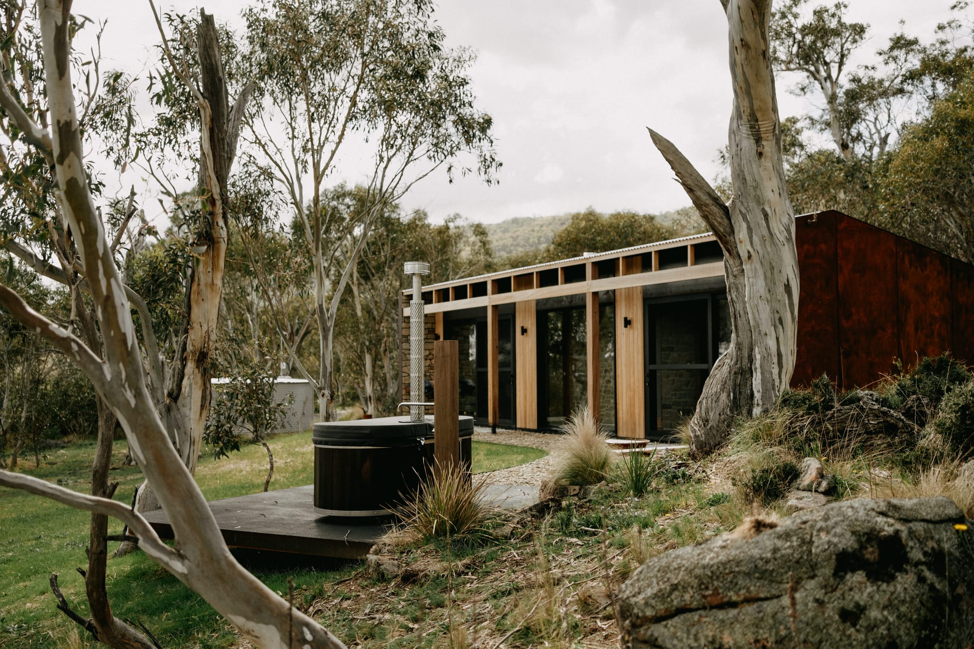 Crafters Eco-Cabins. Image copyright of Crafters. External facade of timber clad cabin with external bath on timber deck. Native Australian bushland surrounds cabin.