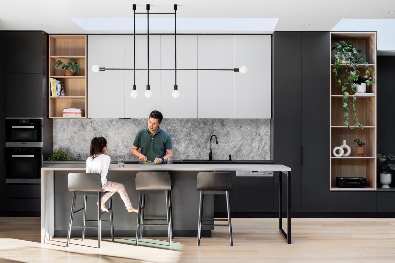 Dickens Street Residence. Photography by Tatjana Plitt. Kitchen with black cabinetry, pale timber floors, stone splashback and concrete island bench.