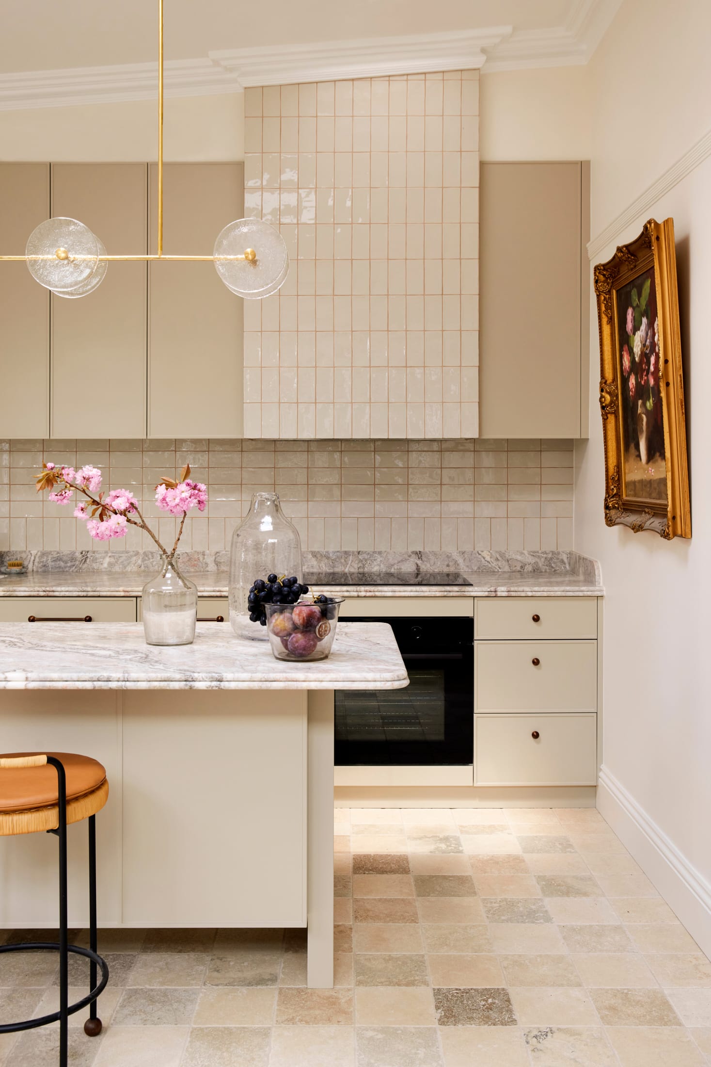 Drummoyne House by studio BARBARA. Photography by Jacqui Turk. Kitchen with checkered travertine floor tiles and glossy subway tiles on splashback. Marble benchtops and abstract gold and glass lighting above island. 