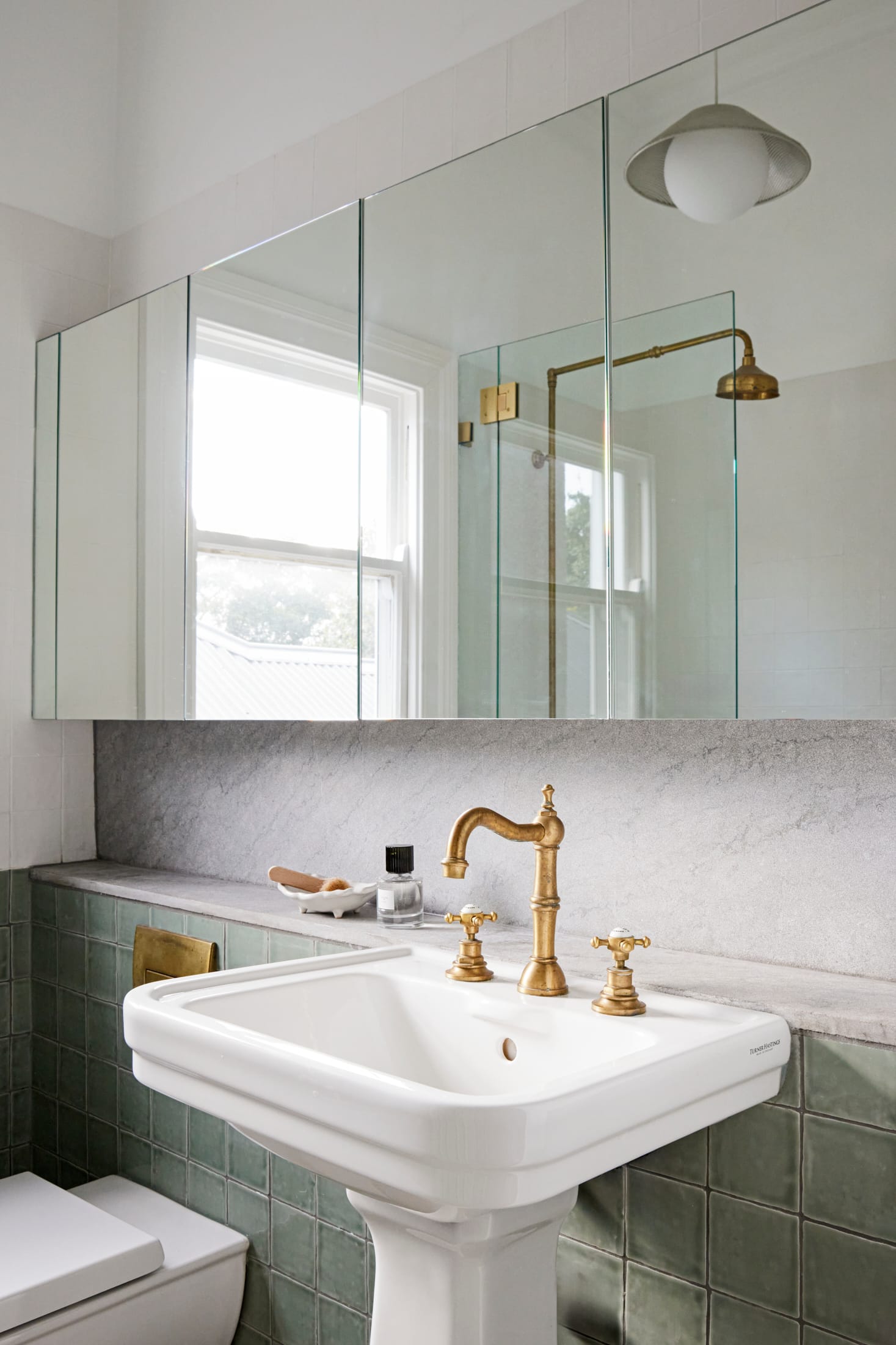 Drummoyne House by studio BARBARA. Photography by Jacqui Turk. Vintage sink in bathroom with gold fixtures and green wall tiles. Overhead wall mirrors and marble splashback.