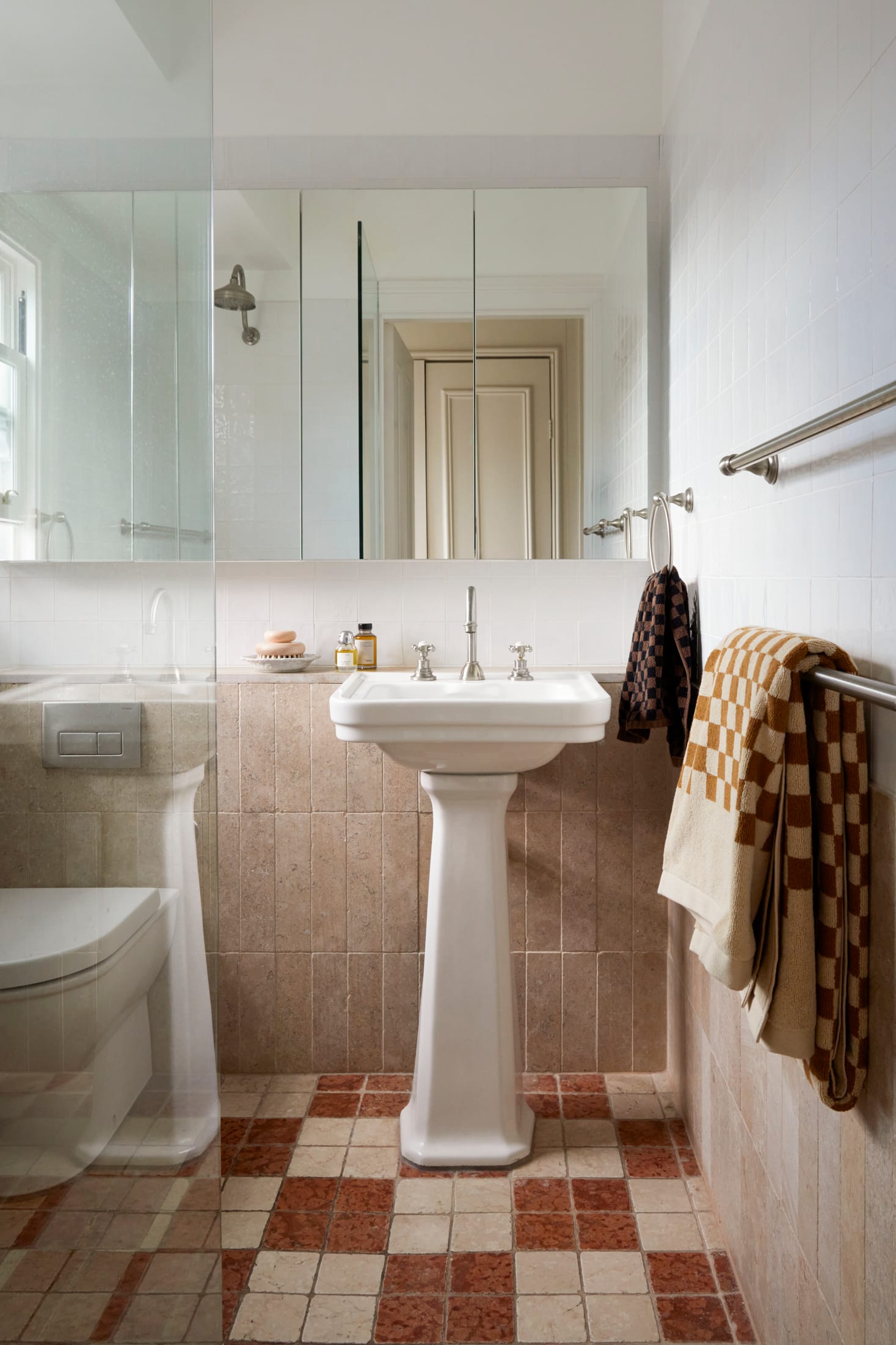 Drummoyne House by studio BARBARA. Photography by Jacqui Turk. Bathroom with heritage stand-alone sink and checkered terracotta and beige travertine floors. Travertine wall tiles and large mirror above sink.
