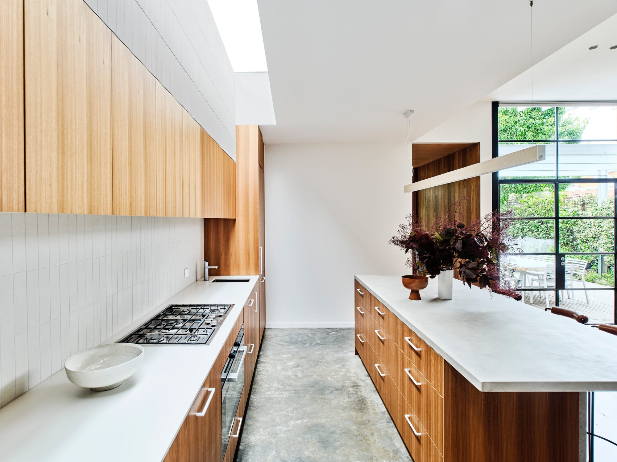 Fitzroy North Residence. Photography by Dean Bradley. Mid century modern inspired kitchen with timber cabinetry and polished concrete floors. White countertops, splashback and walls.