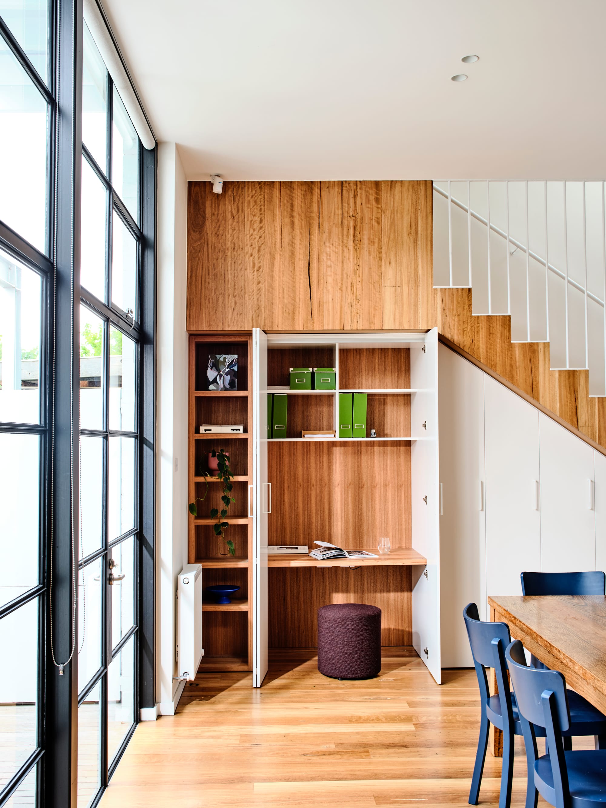 Fitzroy North Residence. Photography by Dean Bradley. Study nook with timber veneer walls, desk and shelving behind white storage doors integrated into timber staircase.