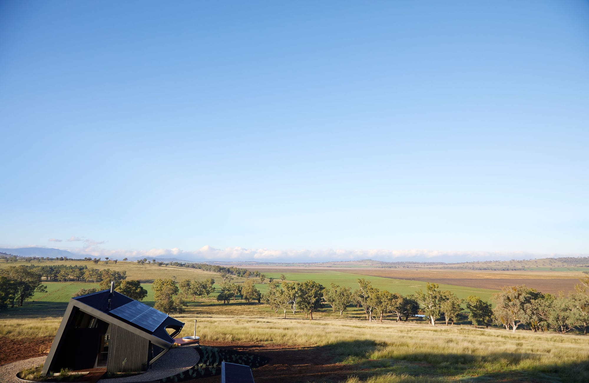 Gilay Estate by Cameron Anderson Architects. Photography by Morning Swim. Black, angled structure in lower left-hand corner, with rolling hills and paddocks around it.