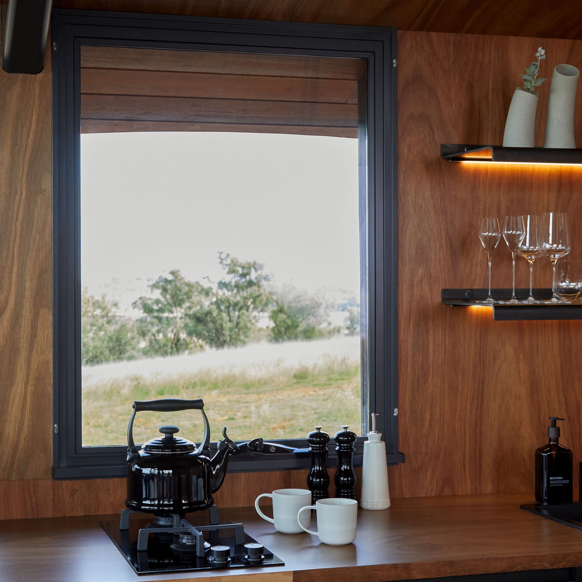 Gilay Estate by Cameron Anderson Architects. Photography by Morning Swim. Kitchen with timber counter and timber veneer walls with window overlooking grassy hills.