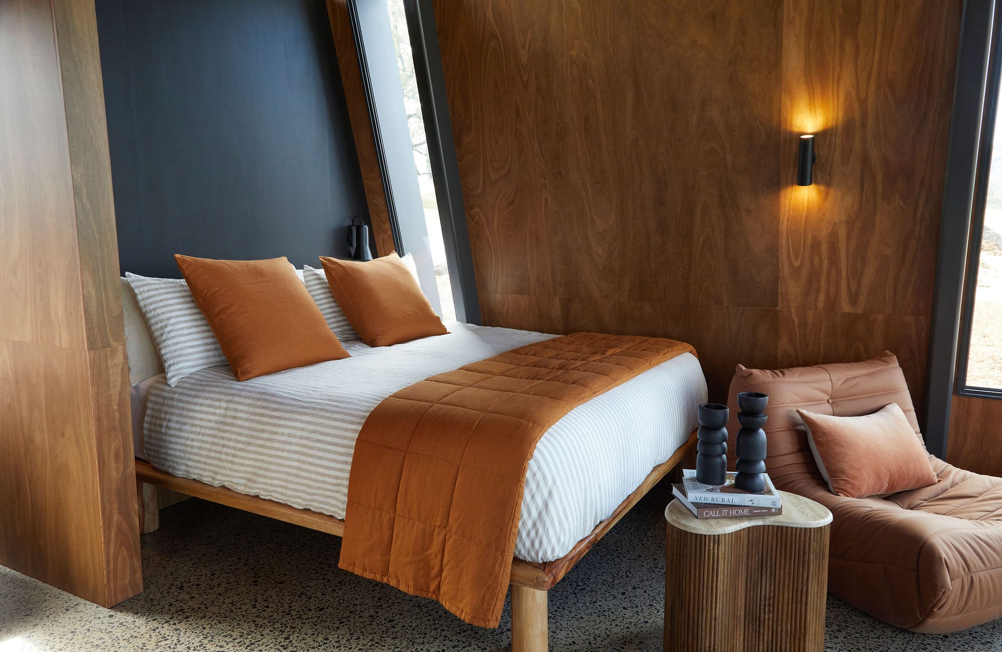 Gilay Estate by Cameron Anderson Architects. Photography by Morning Swim. Bed with white and grey striped linen and orange throw pillows and rug. Polished concrete floors and timber veneer walls.