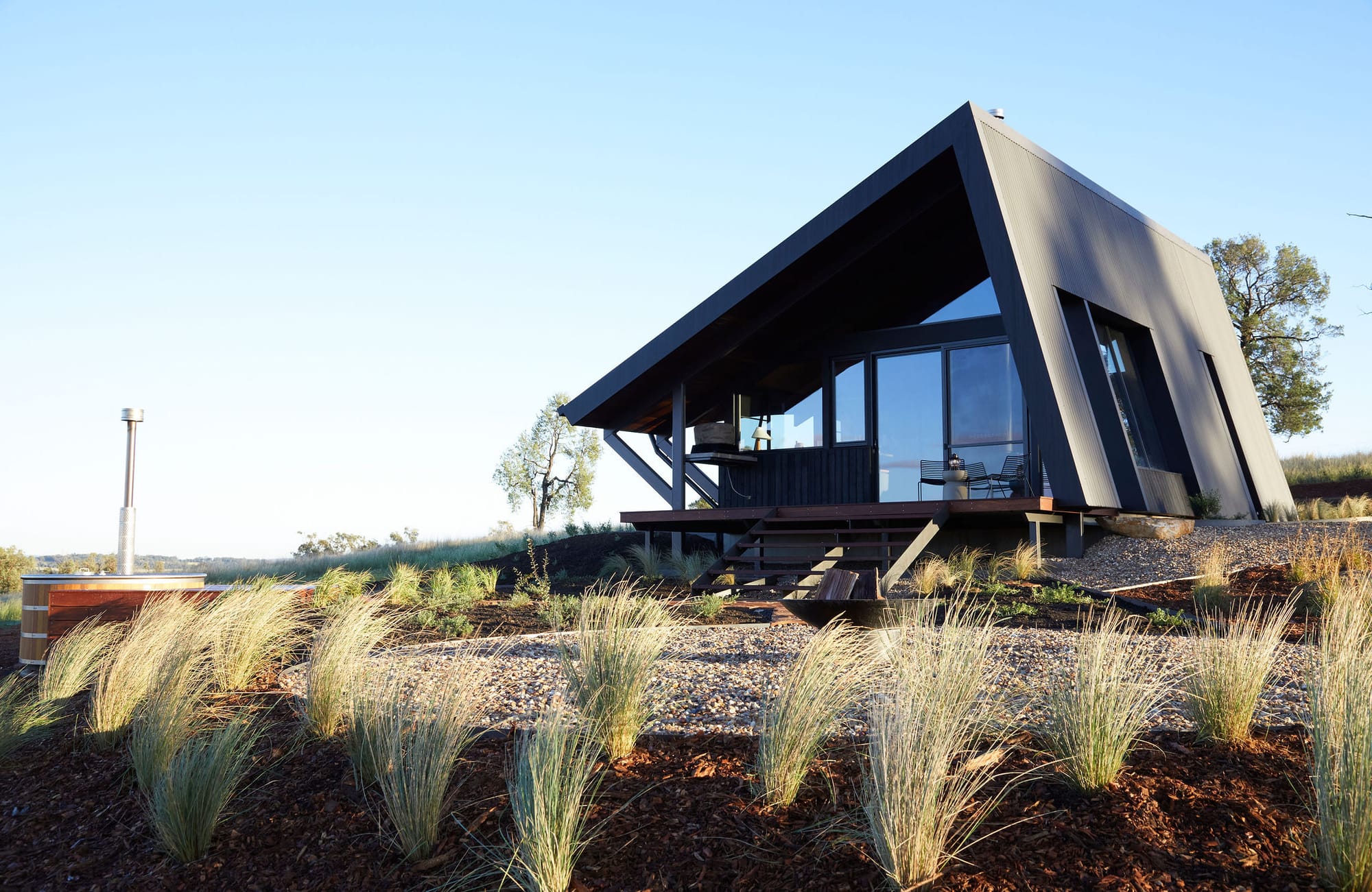 Gilay Estate by Cameron Anderson Architects. Photography by Morning Swim. Angled building with black finish in middle of rocky hillscape. Native grasses growing in foreground.