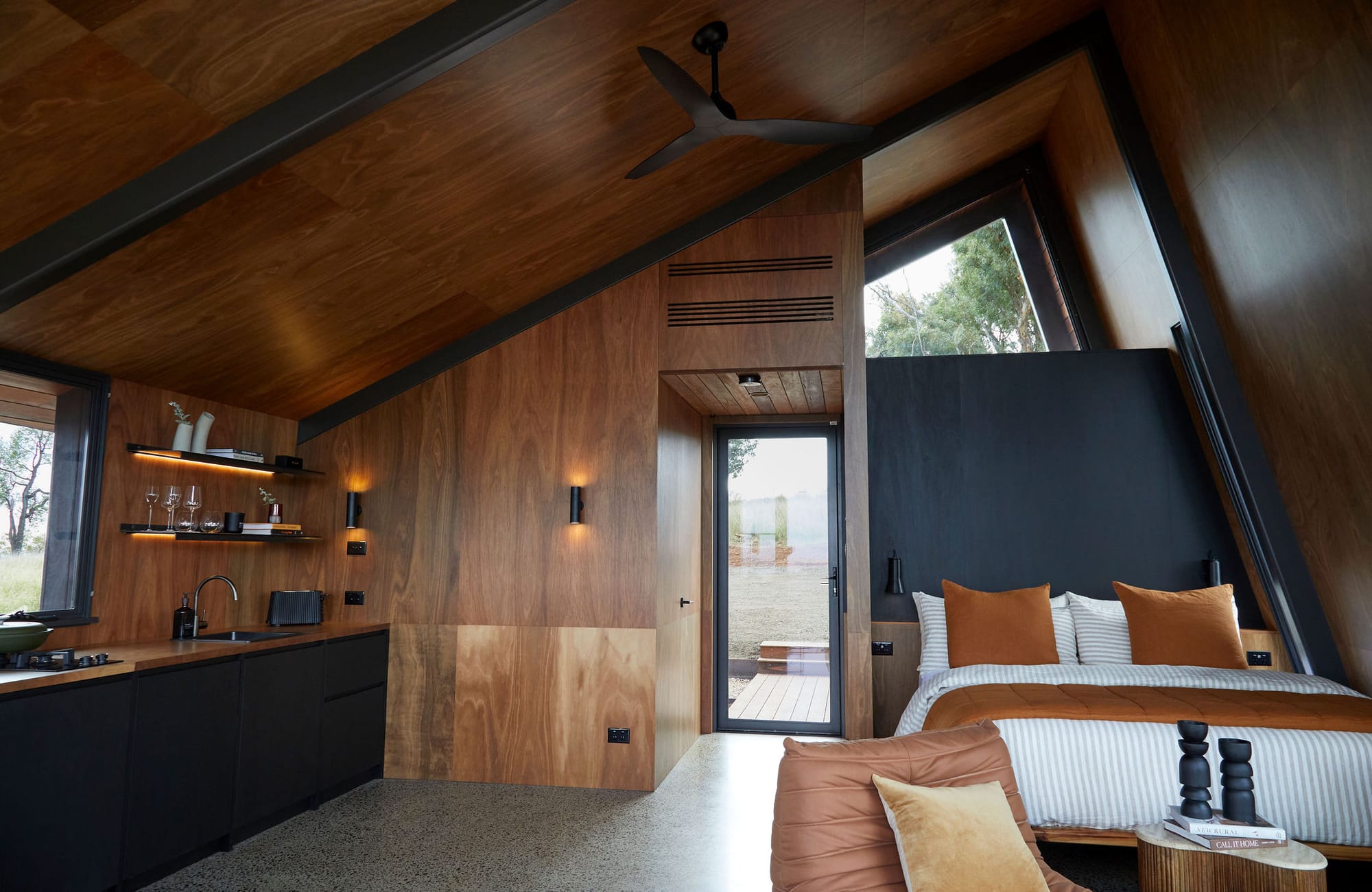 Gilay Estate by Cameron Anderson Architects. Photography by Morning Swim. Interior of small building with timber veneer walls and ceilings. Angled ceilings with black support beams and polished concrete floor.