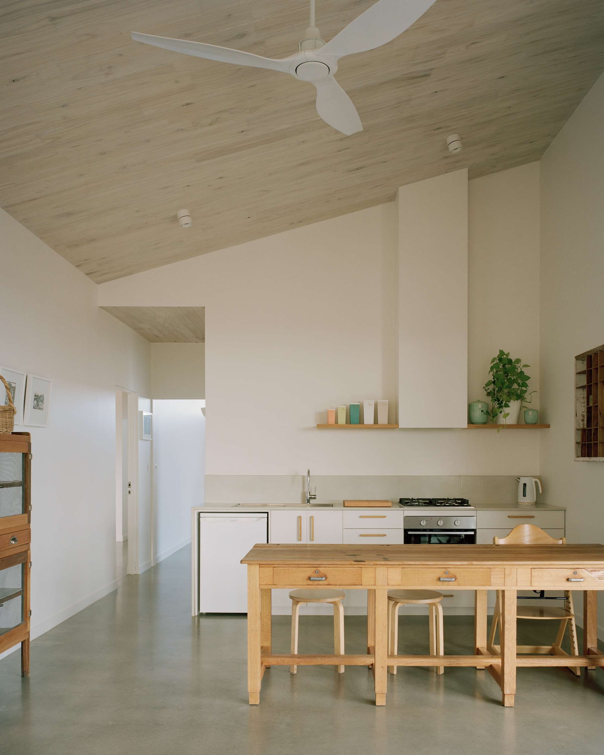 Heather's Off-Grid House by Gardiner Architects. Photography by Rory Gardiner. Kitchen with polished concrete floors and high angled ceiling with timber finish and white walls. Timber island bench with stools. 