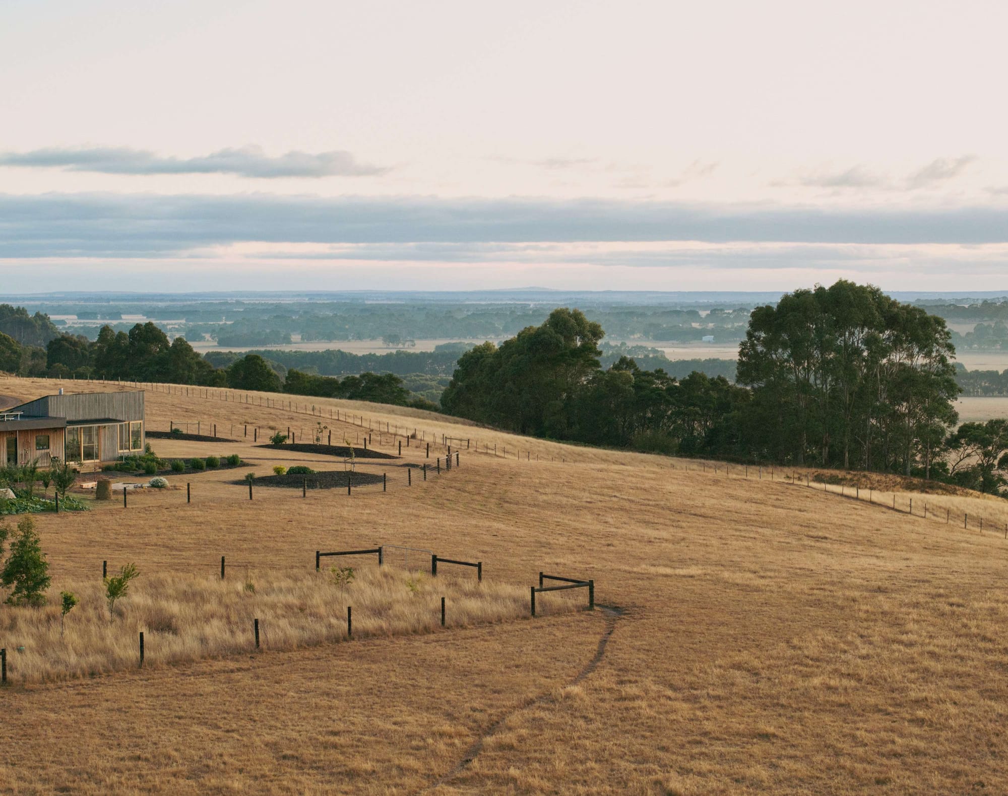 Heather's Off-Grid House by Gardiner Architects. Photography by Rory Gardiner. Dry and barren paddock with timber clad farmhouse in left edge of frame. 