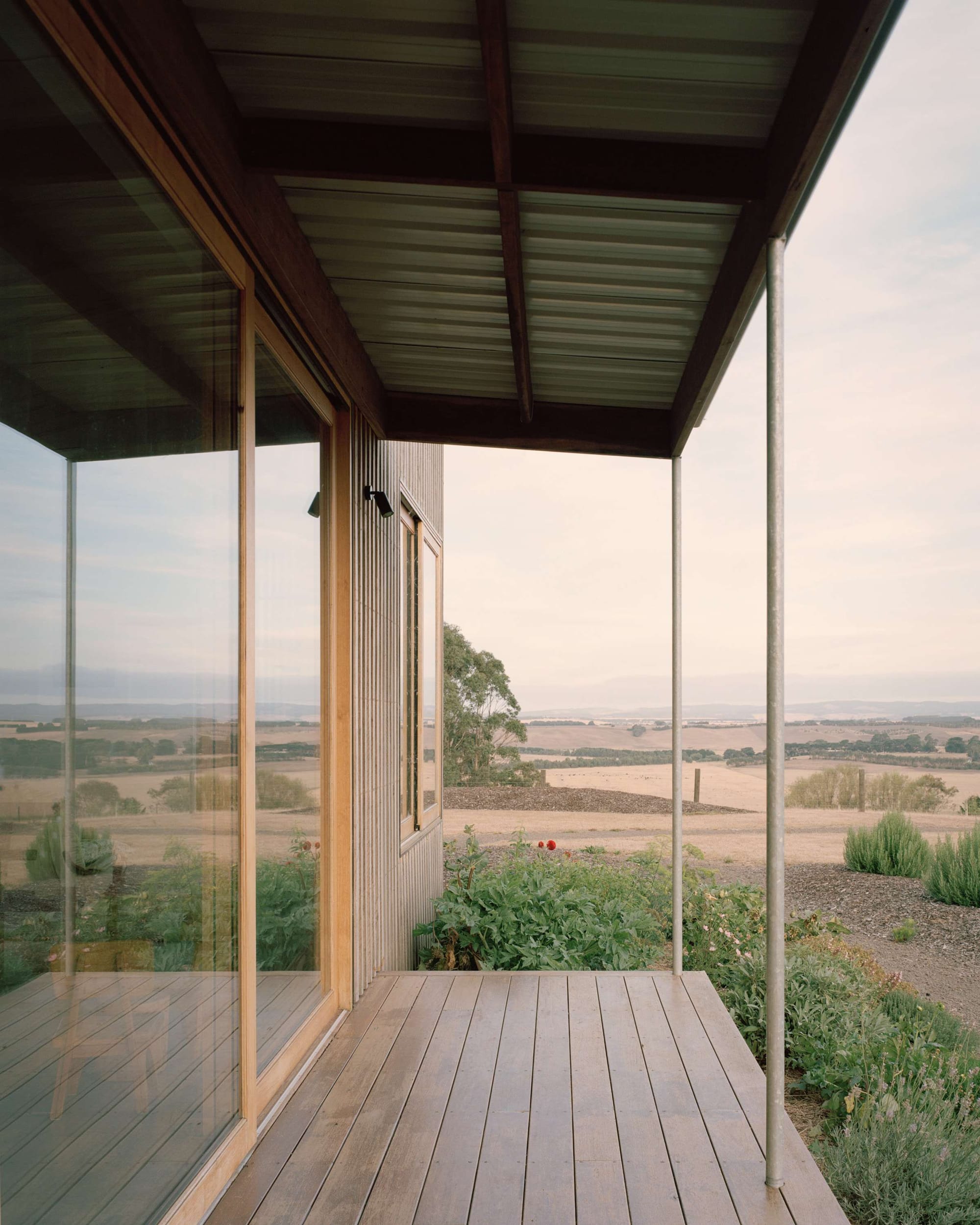 Heather's Off-Grid House by Gardiner Architects. Photography by Rory Gardiner. Timber verandah overlooking barren and dry paddocks. Timber clad walls on home and tin roof. 