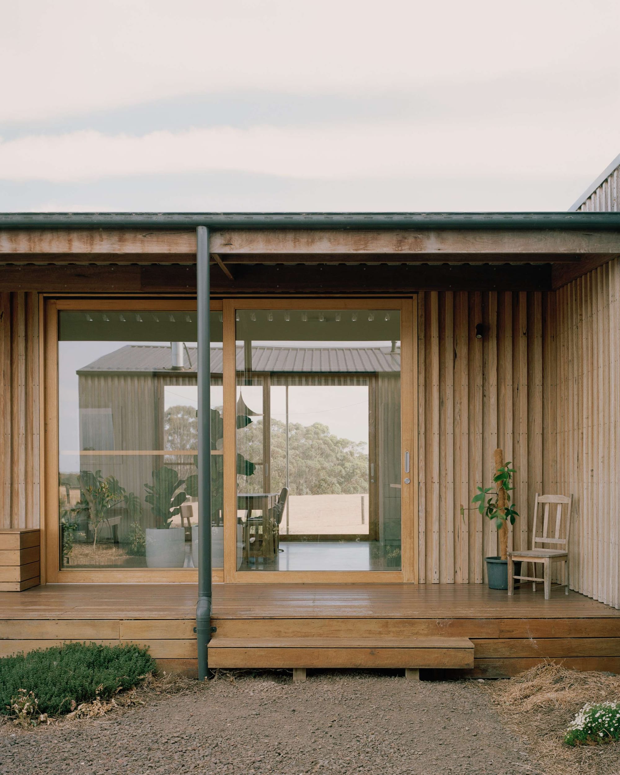 Heather's Off-Grid House by Gardiner Architects. Photography by Rory Gardiner.  Facade of timber clad home with small timber verandah and glass sliding door. Gravel ground. 