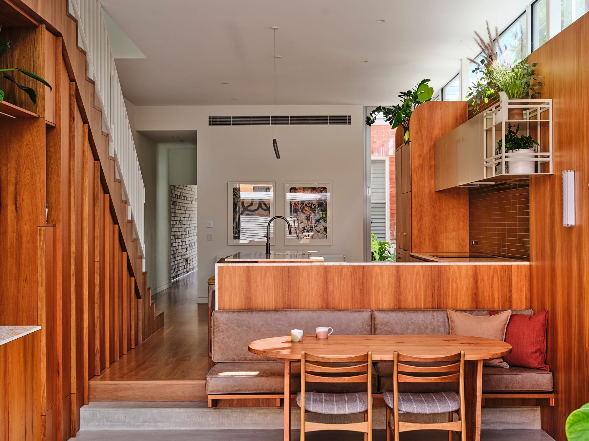 House Northroy by True Story. Photography by Dean Bradley. Sunken breakfast nook with brown leather bench seat and timber table. Timber kitchen and stairs on level above.
