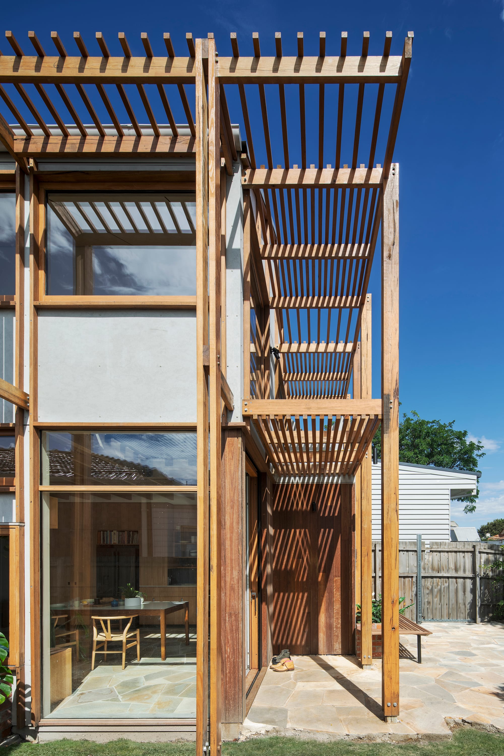 An exterior shot of the side elevation of the house showing timber detail work and a glimpse into the dining and kitchen space