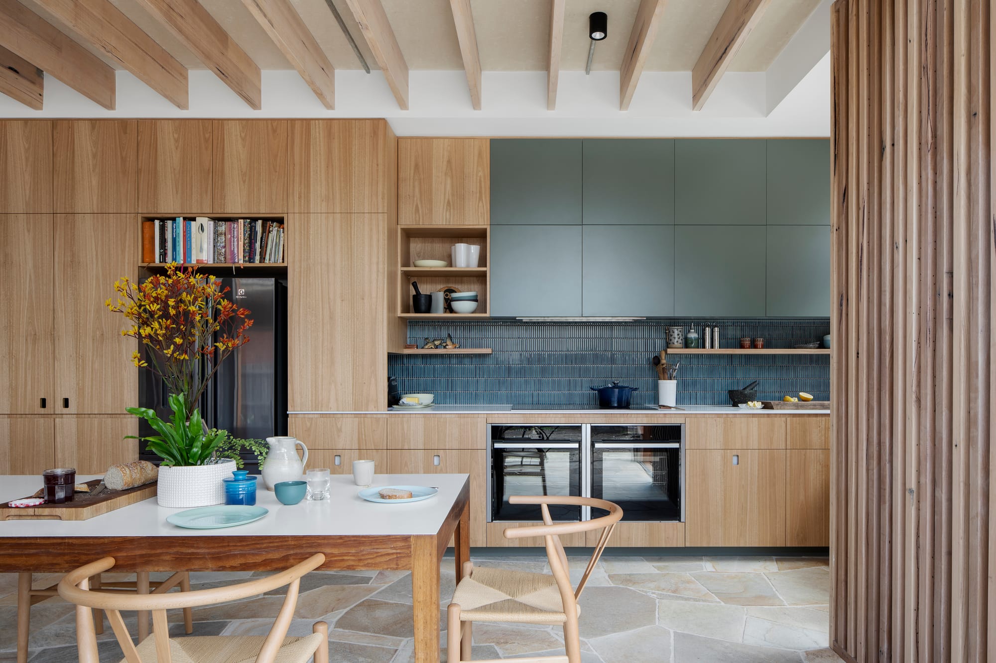 An interior shot of the kitchen and dining space showing timber veneer joinery and a timber dining set in the foreground