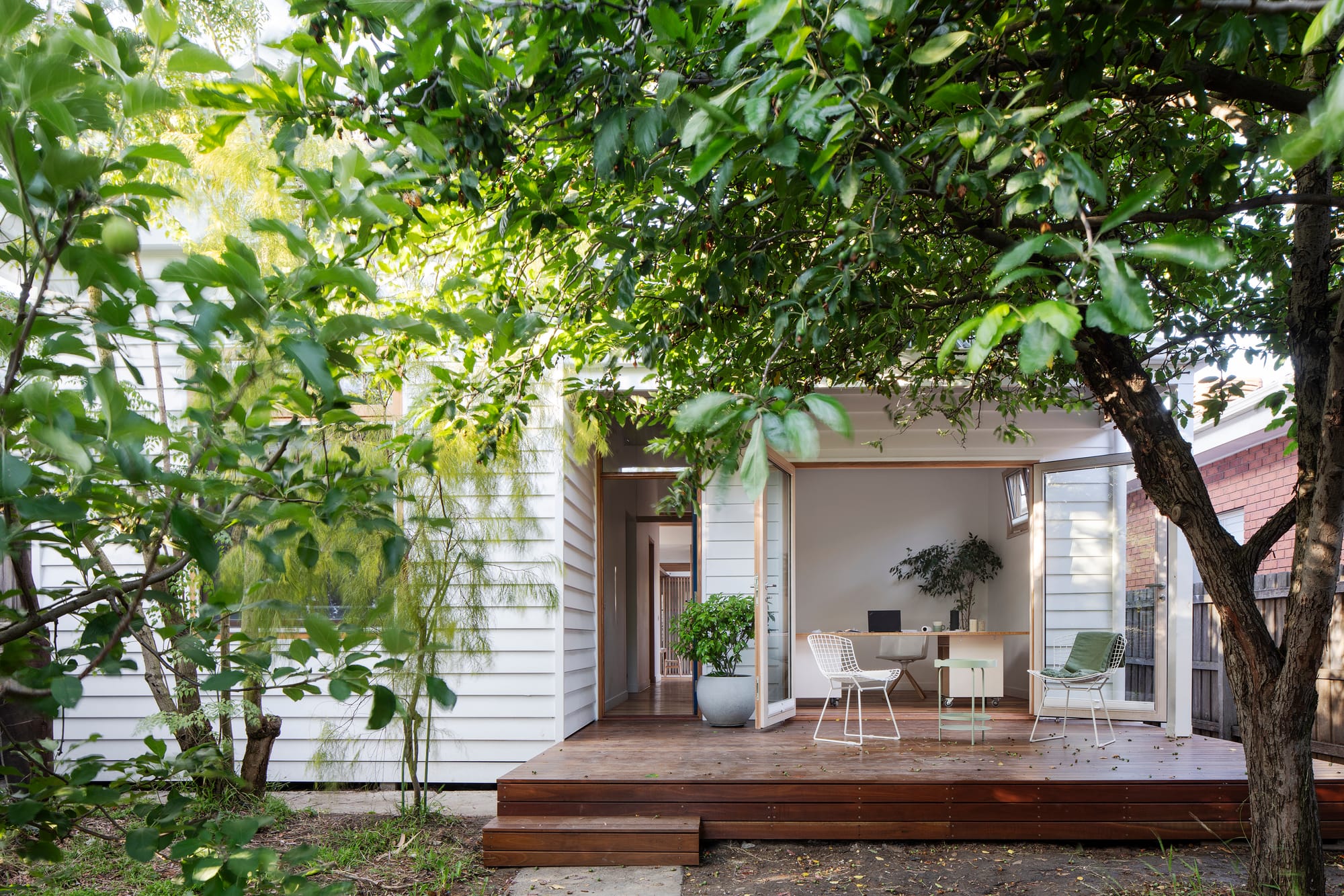 An exterior shot showing the house amongst the trees and a timber deck with outdoor seating