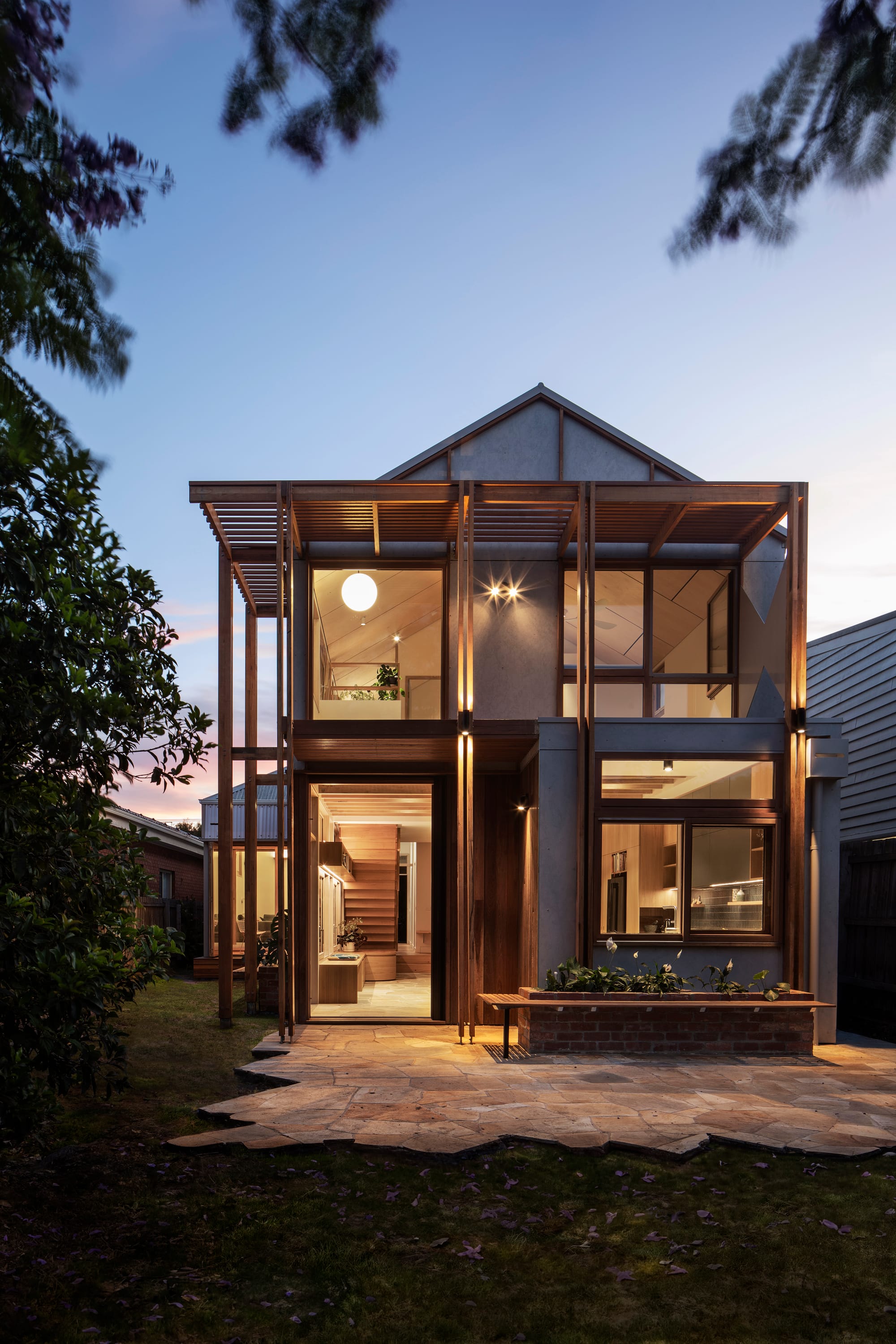 An exterior shot of the rear of the house at dusk with internal lights on