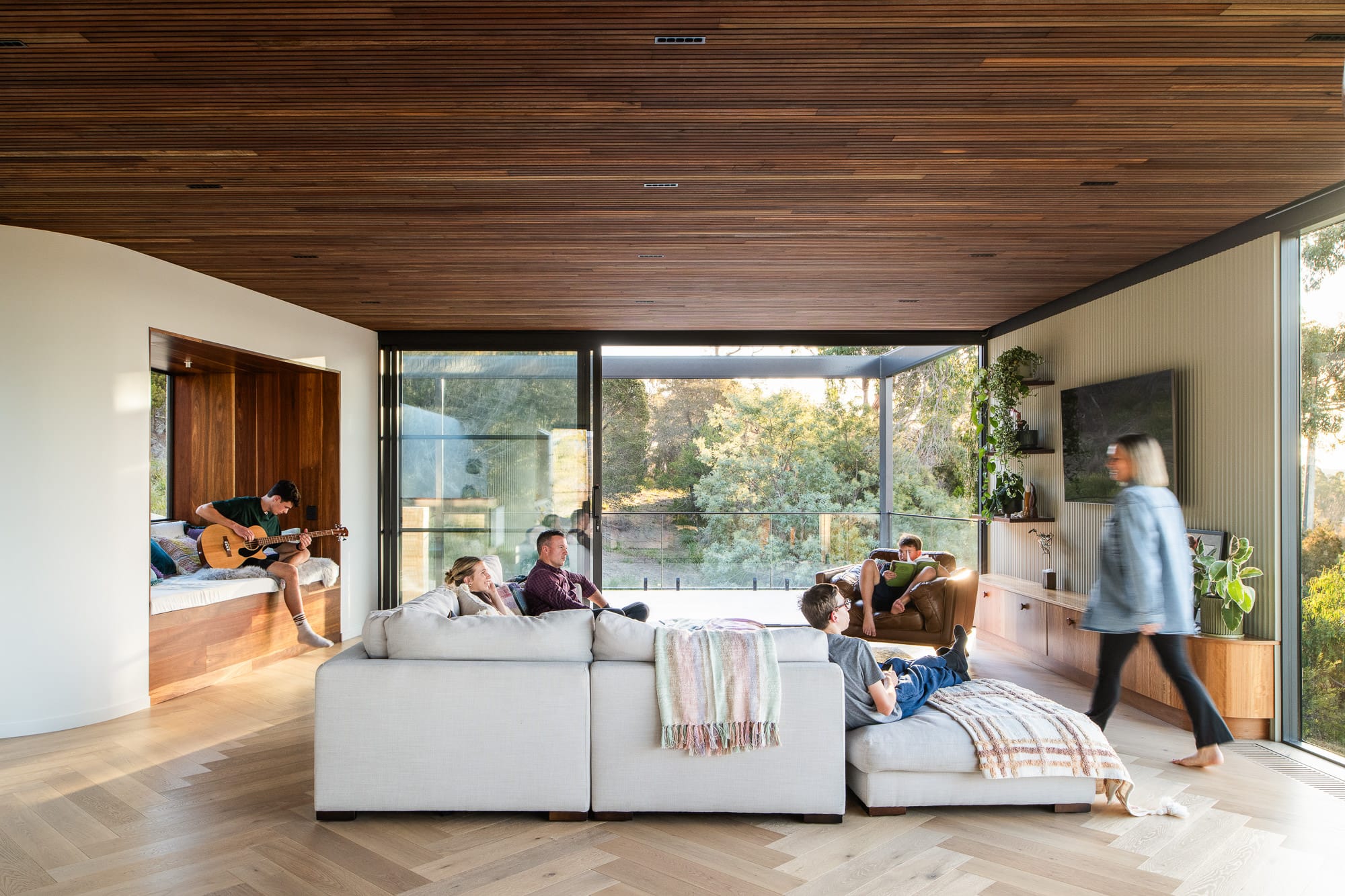 Mortlock Timber Series: The Milldam. Photography by Anjie Blair. Living space with white modular lounge and timber herringbone floors. Timber clad ceiling and windows overlooking bushland. 