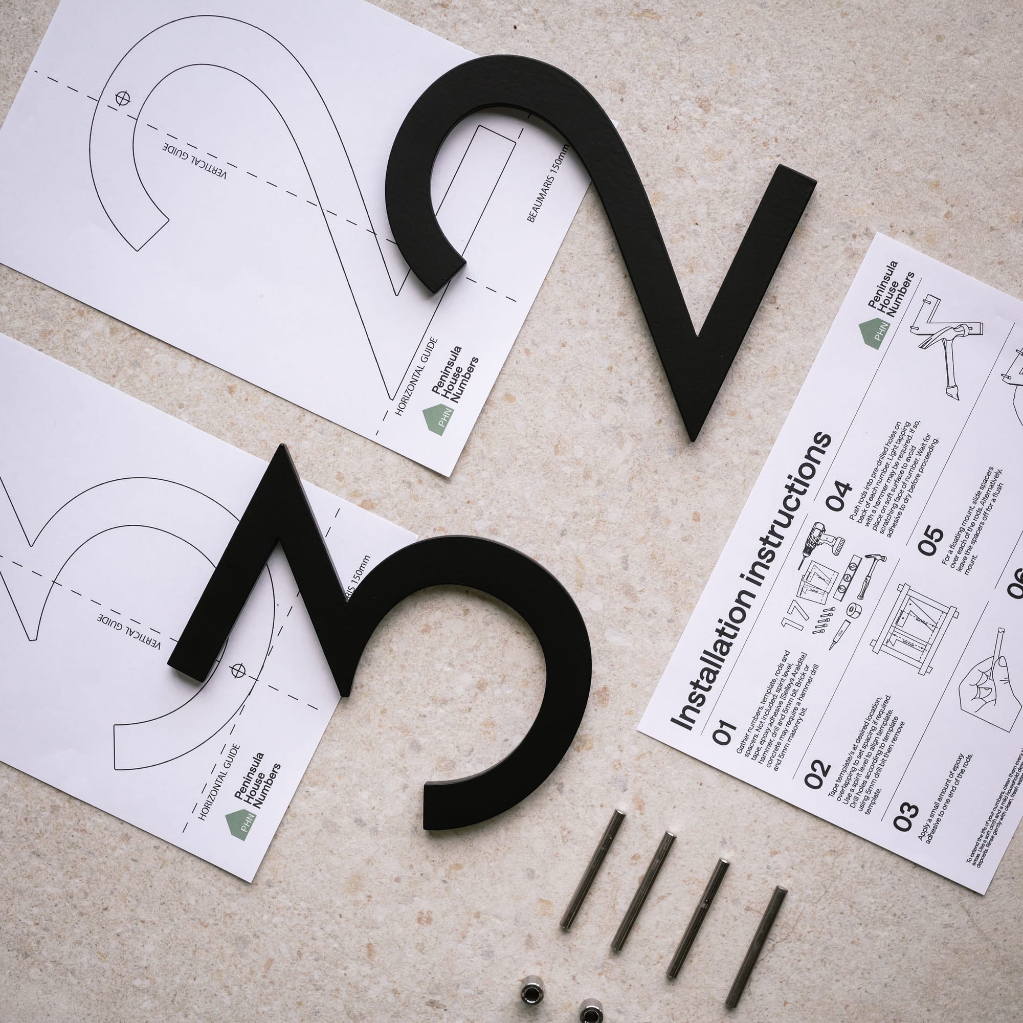 Peninsula House Numbers. Image copyright of Peninsula House Numbers. Black metal number 3 and 2 on top of installation papers.