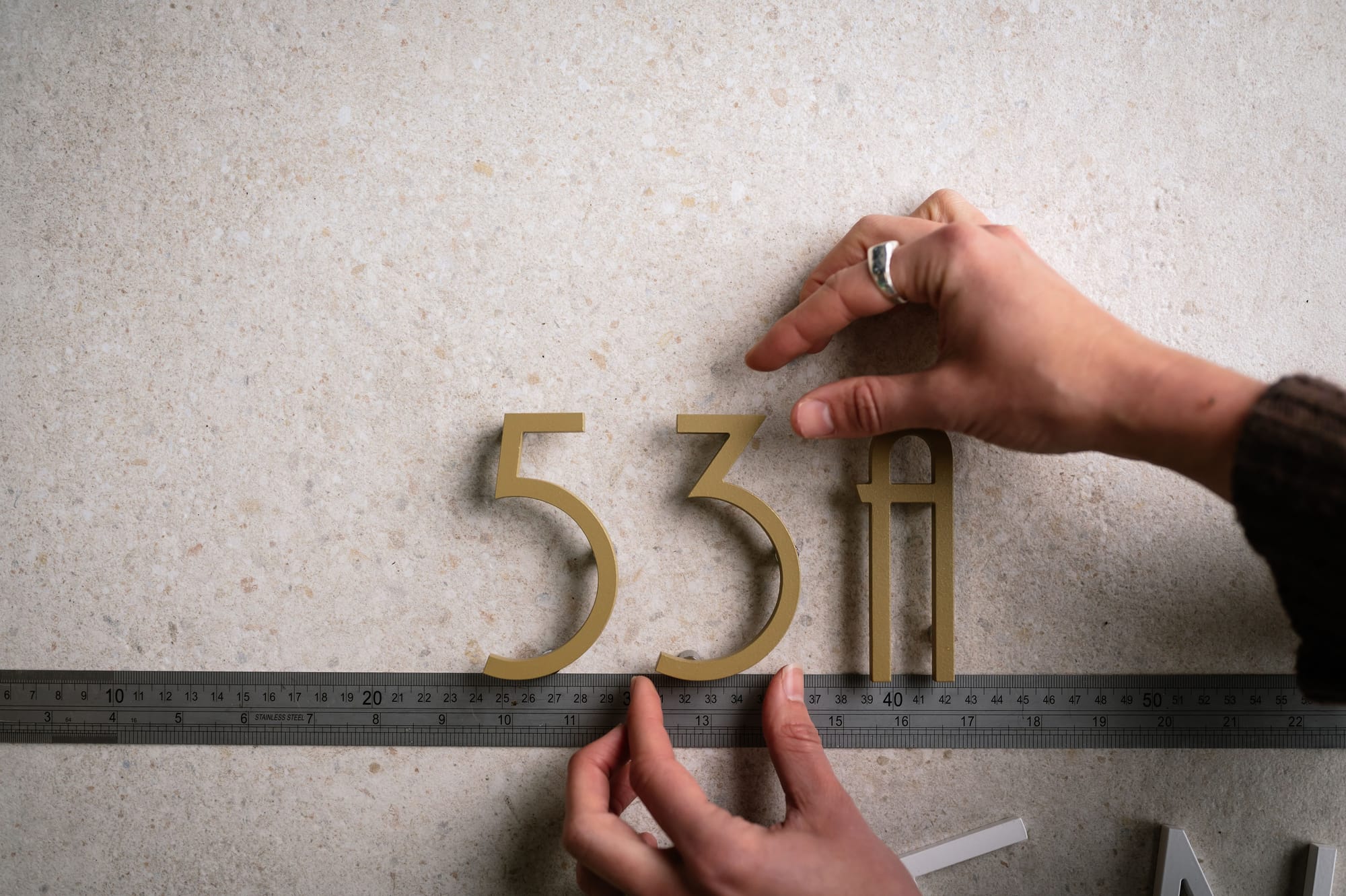 Peninsula House Numbers. Image copyright of Peninsula House Numbers. Brass house numbers being arranged in line above ruler.
