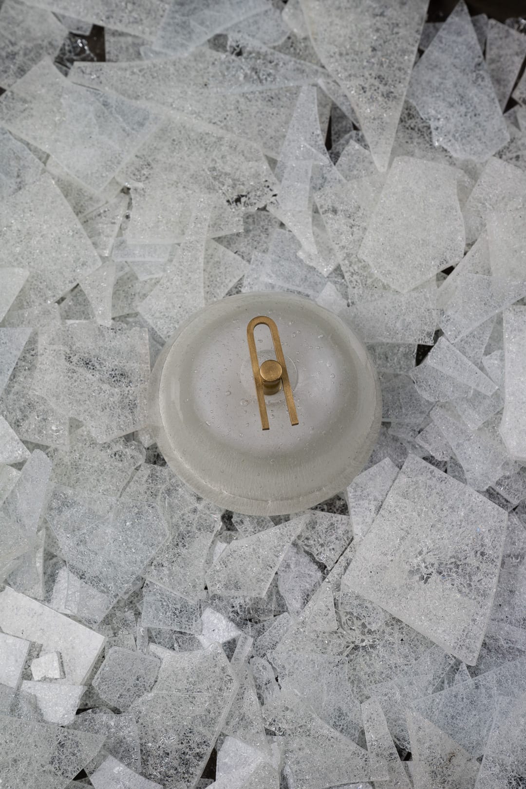 Point Five by South Drawn. Image copyright of South Drawn. Domed light sitting on bed of crackled glass shards. Light has gold pin on front.