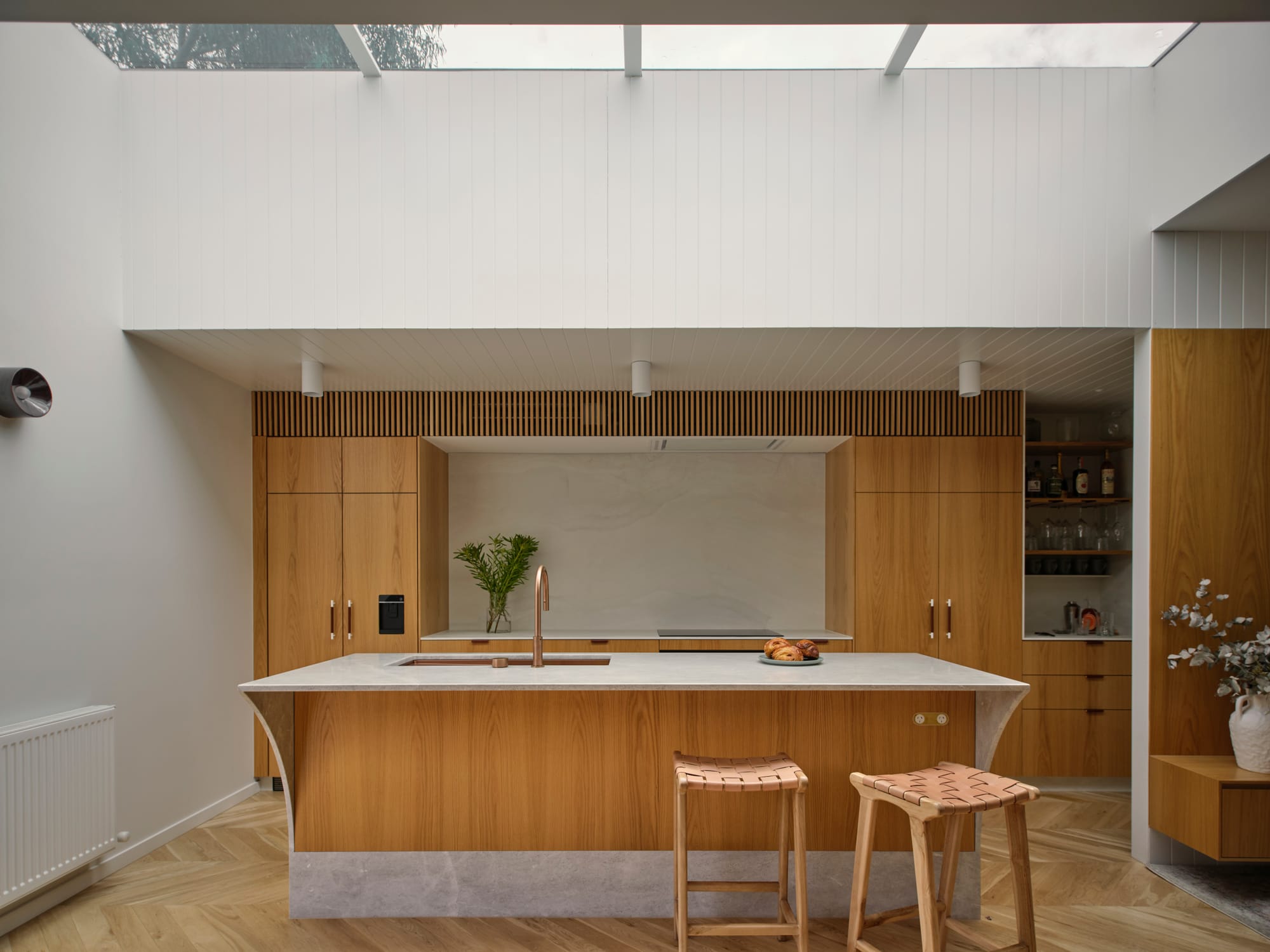 ZigZag House by True Story. Photography by Dean Bradley. Kitchen with warm timber cabinetry and timber herringbone floors. Overhead skylight, white walls.