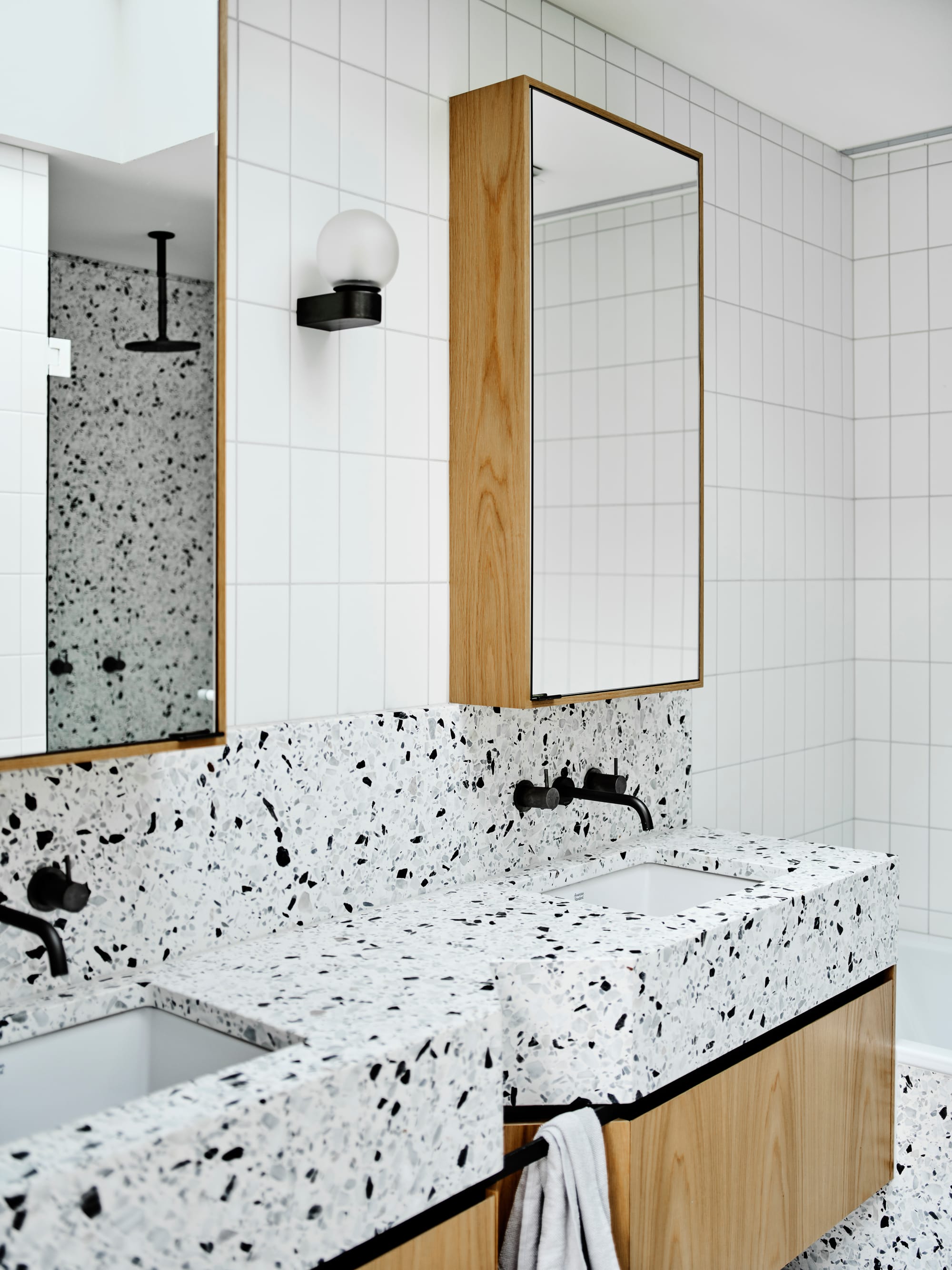 ZigZag House by True Story. Photography by Dean Bradley. Bathroom with white and black speckled terrazzo countertops and splashback. Timber cabinetry. White tiled walls and timber framed mirrors.
