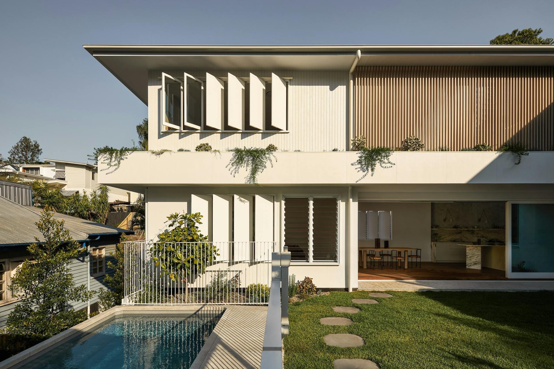 Hazlewood House by Favell Architects. Photography by Andy MacPherson. Rear facade of double storey white clad home with green backyard and pool.