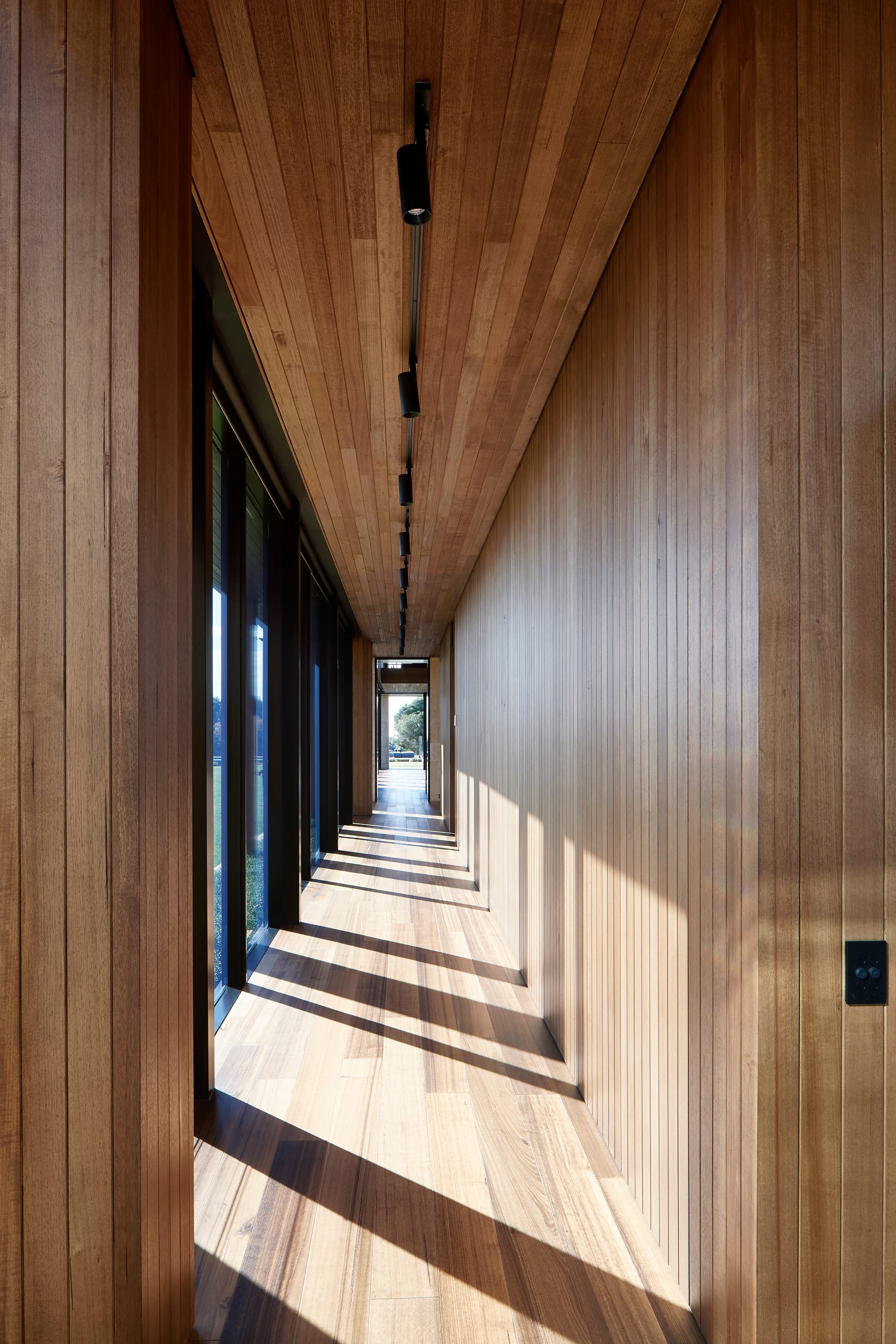 Tasmanian Timber in Flinders Residence by Abe McCarthy. Photography by Shannon McGrath. Floor-to-ceiling windows in tall, arched shape bordered by angled timber clad ceiling. Timber clad floors and black freestanding fireplace.