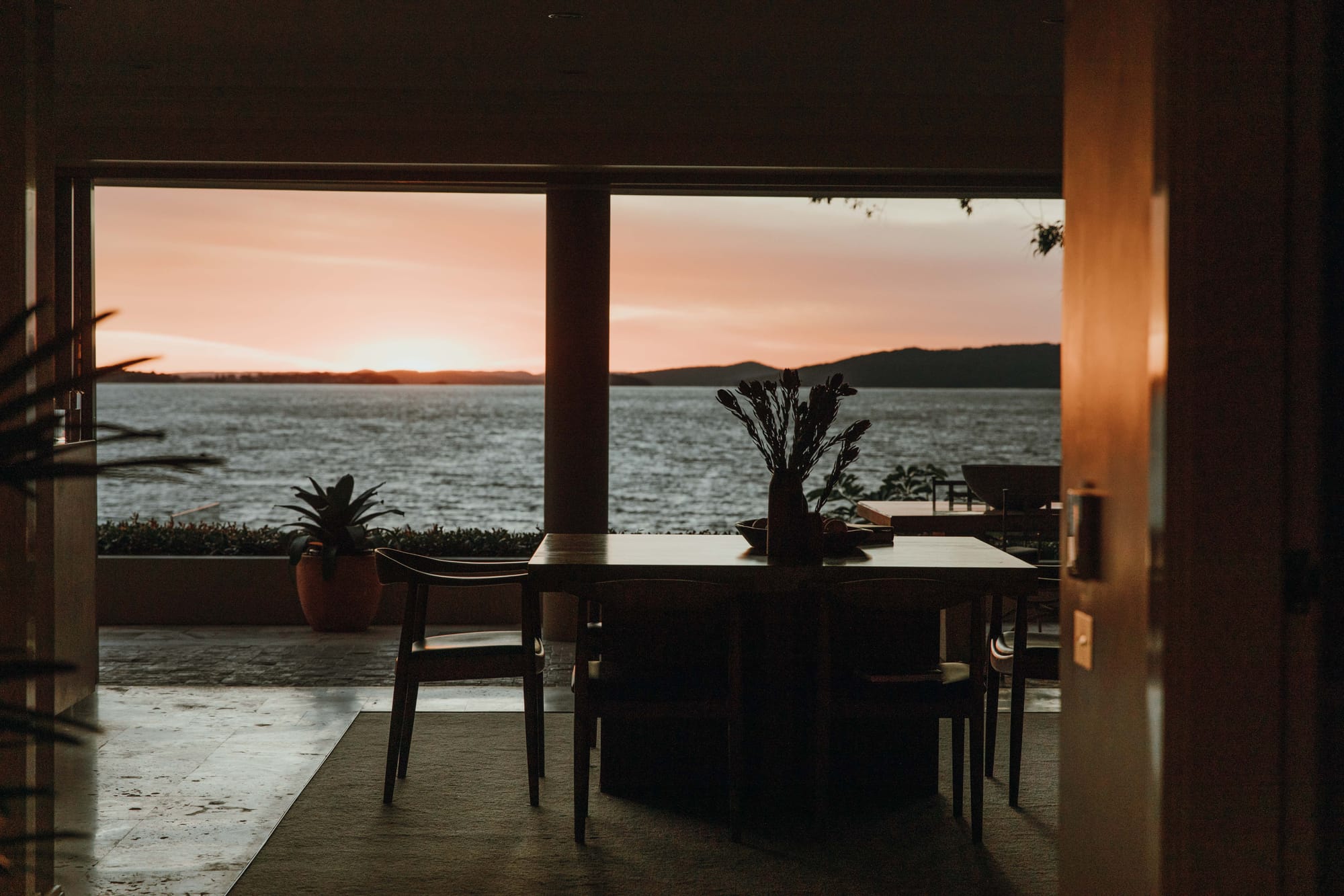 Amarna Luxury Beach Resort. Photography by Will Salkeld. Outdoor dining area overlooking views of open harbour and hills in background at sunset. 