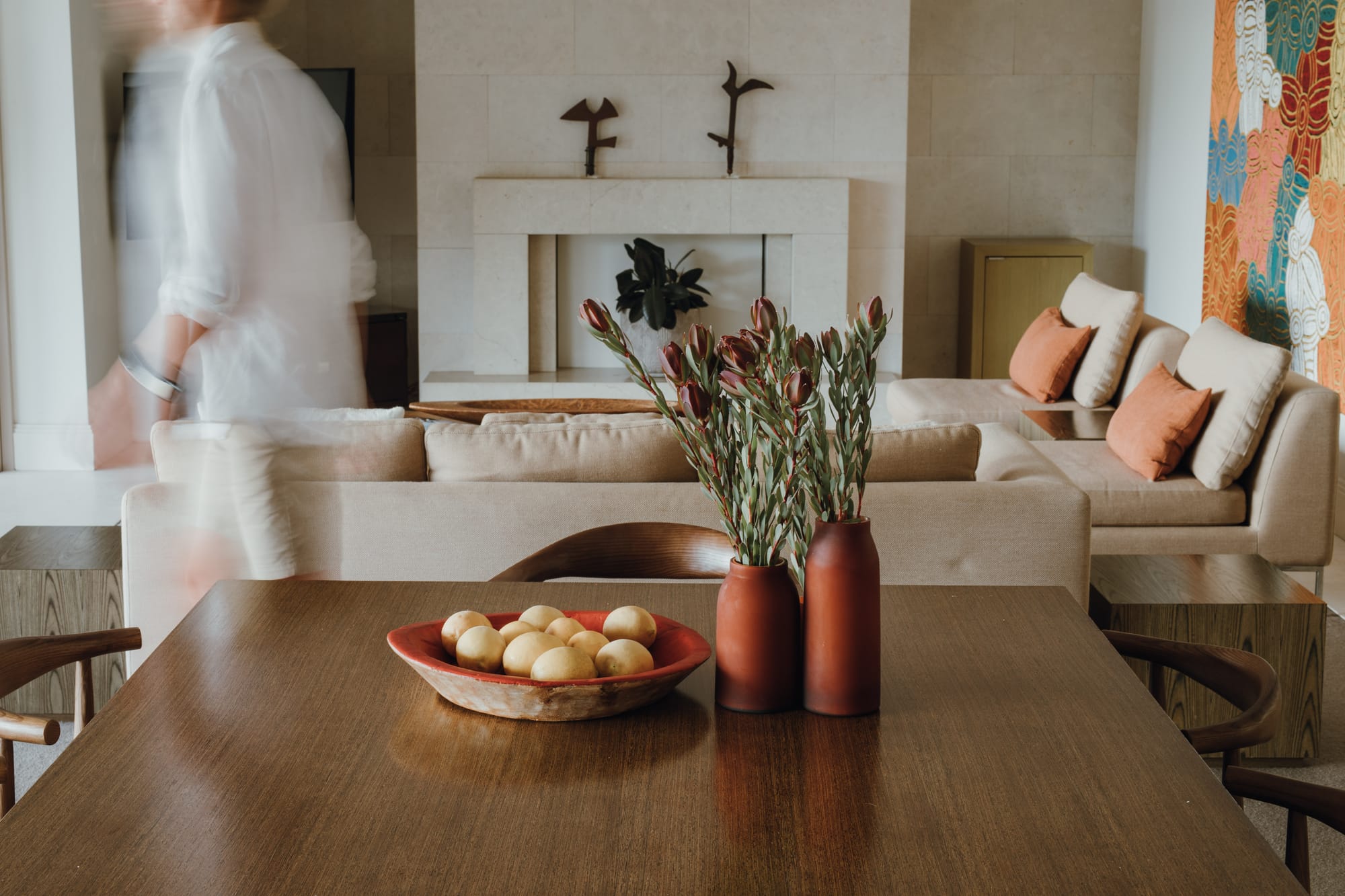 Amarna Luxury Beach Resort. Photography by Will Salkeld. Open living and dining area with timber dining table in foreground and light modular lounges in background. White stone fireplace and stone walls. 