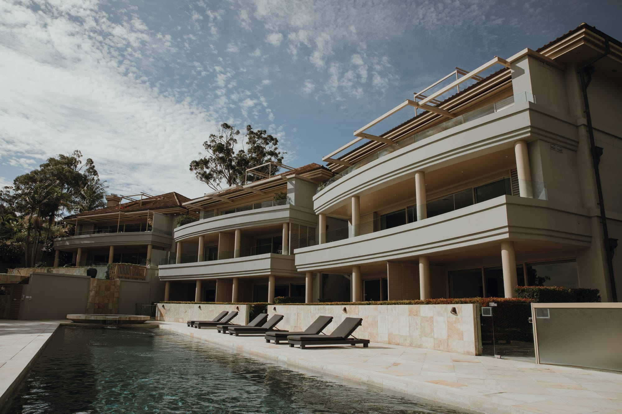 Amarna Luxury Beach Resort. Photography by Will Salkeld. Facade of multi-story building with tiled pool area at the front, with multiple chaise lounges alongside pool. 