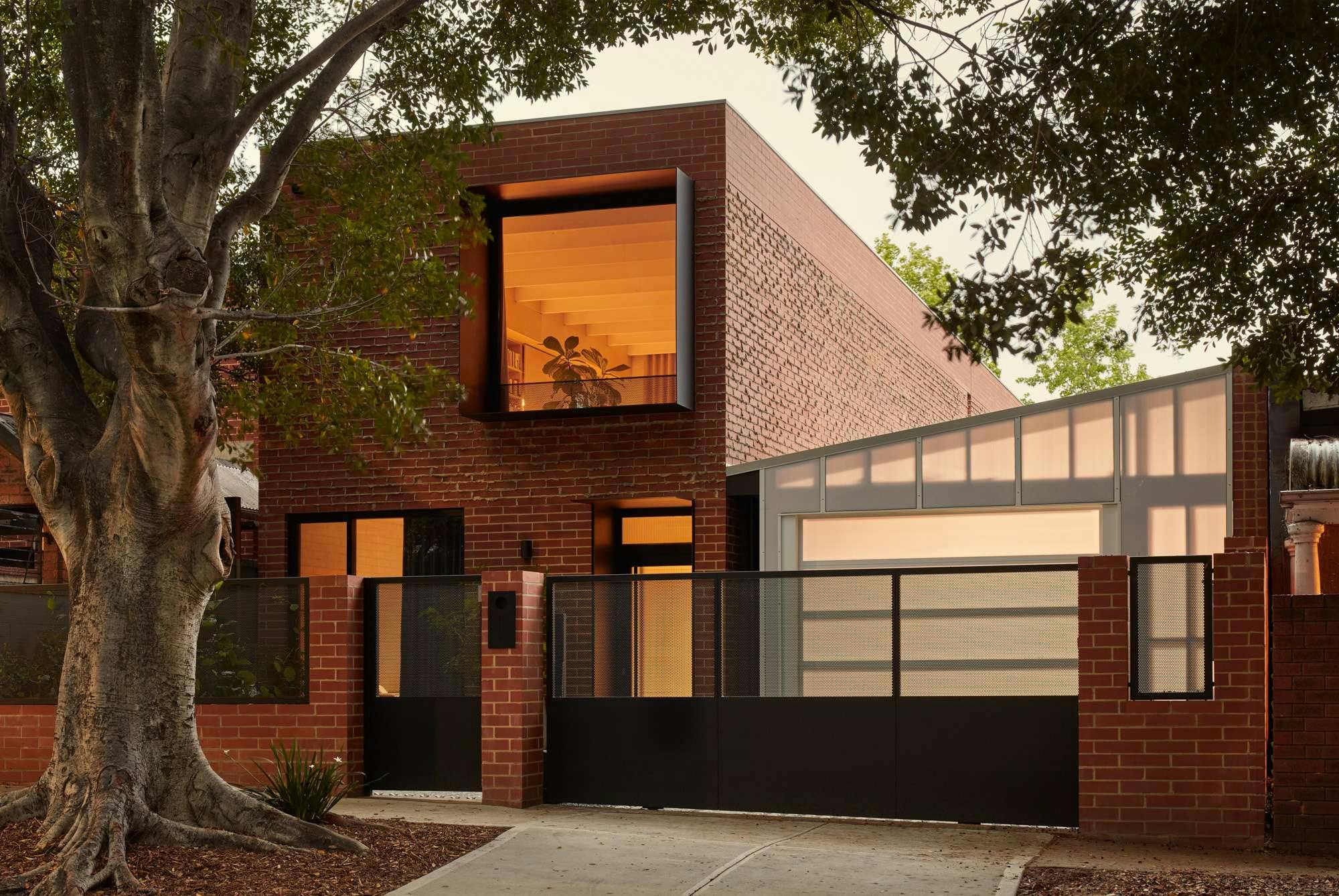Brick House by Studio Roam. Photography by Jack Lovel. Street facade of double storey brick home with warm light emitting windows. 