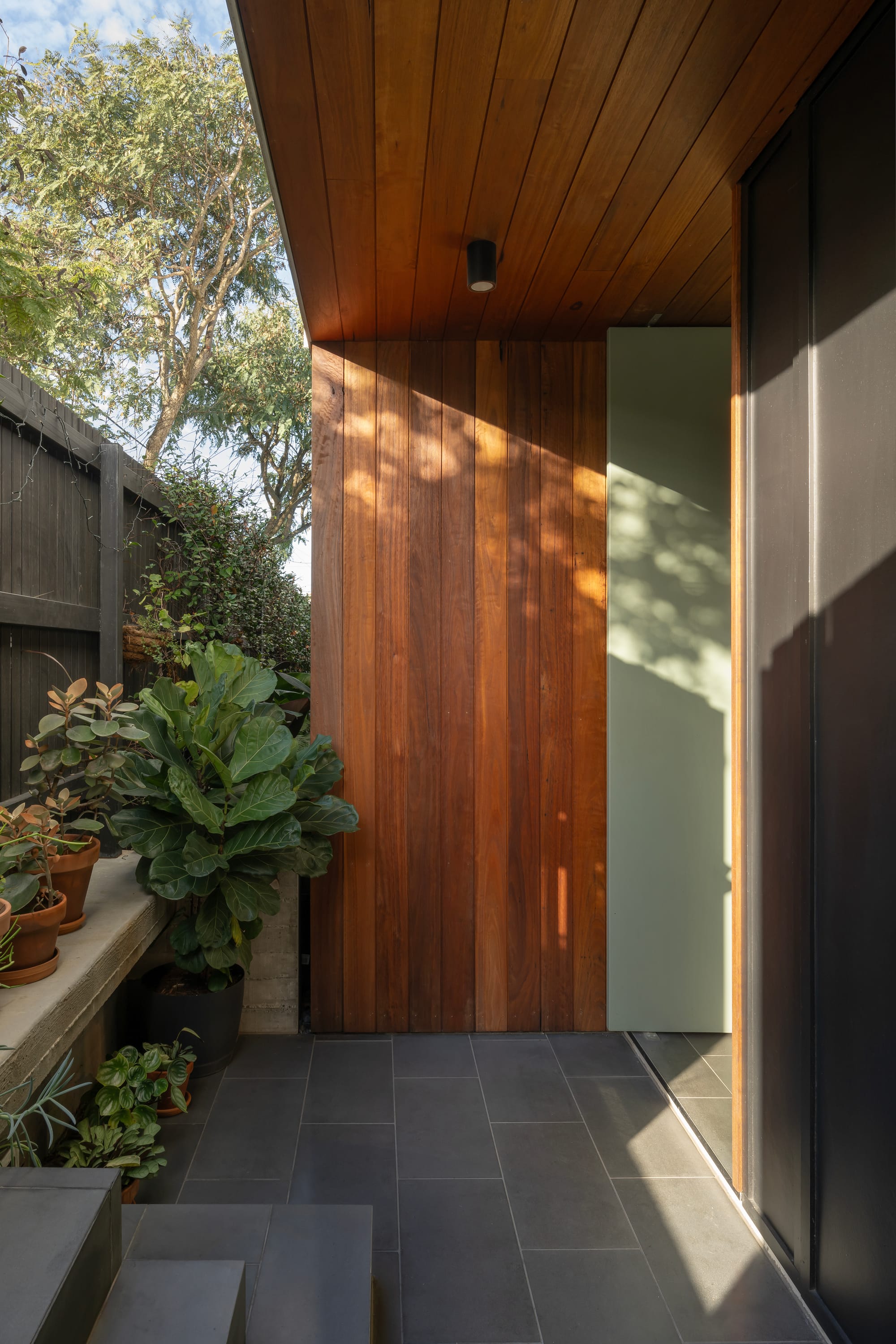 Cornerstone by Loupe Architecture. Photography by Alanna Jayne McTiernan. Outdoor entrance with bluestone floors and steps and solid timber clad door alongside concrete garden bed. 