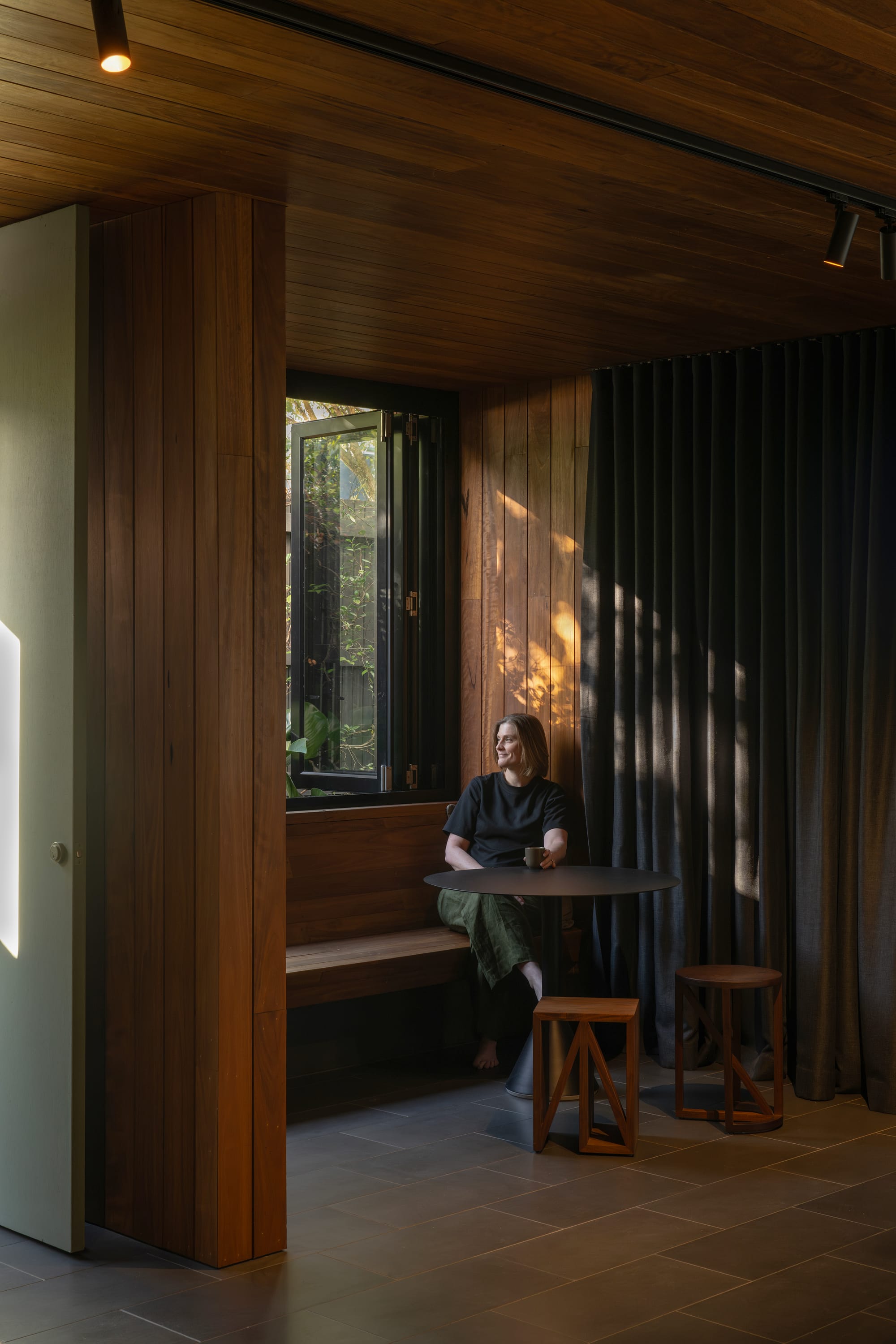 Cornerstone by Loupe Architecture. Photography by Alanna Jayne McTiernan. Reading nook with timber bench seat, black dining table, black curtains and stone floors. 