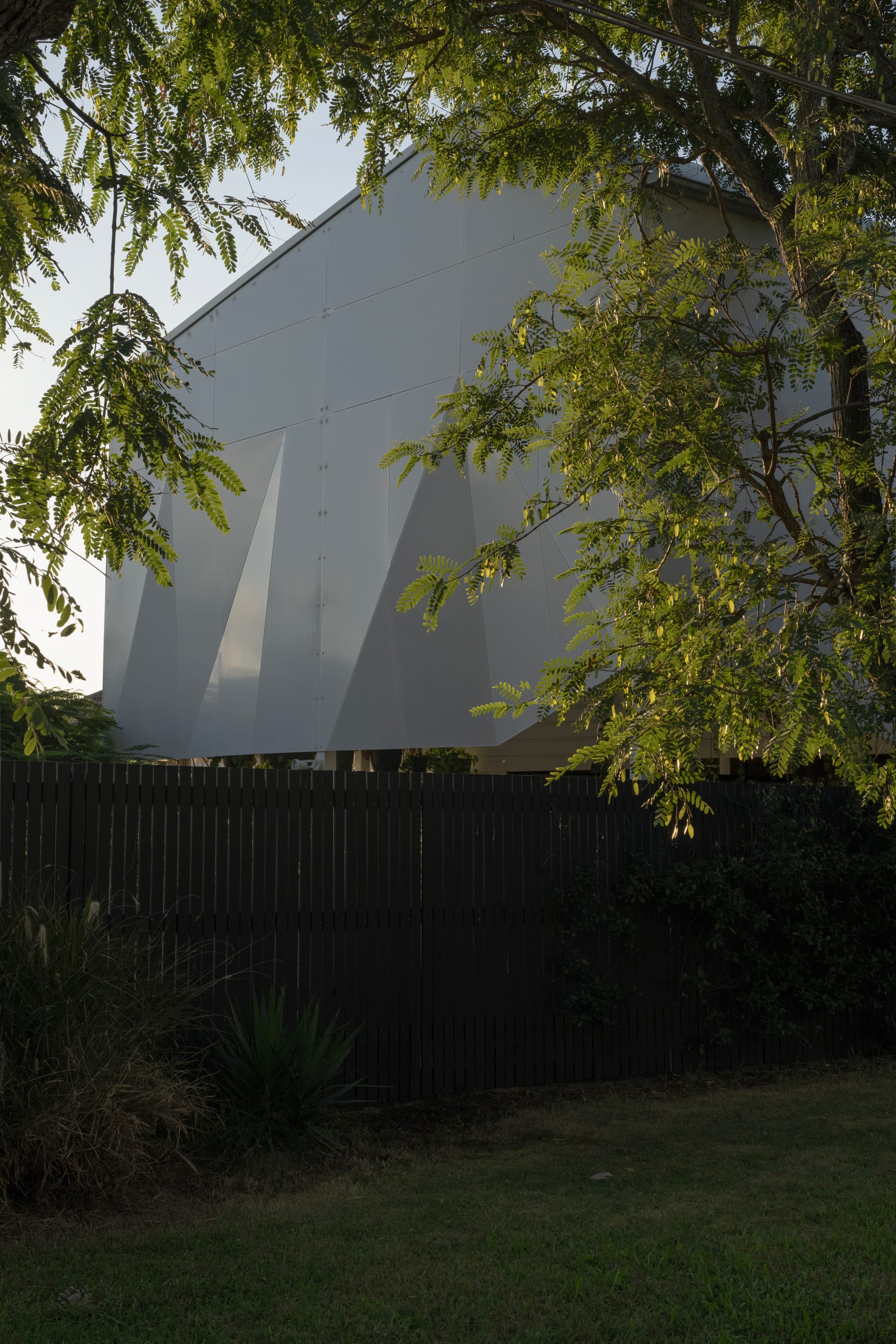 Cornerstone by Loupe Architecture. Photography by Alanna Jayne McTiernan. Rear facade of modern white metal home with black timber fence and hanging ferns. 