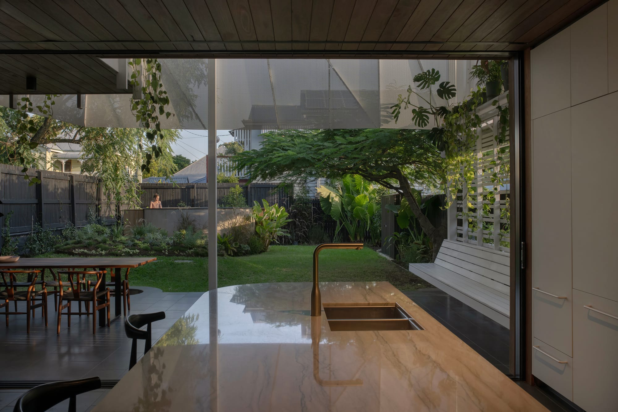 Cornerstone by Loupe Architecture. Photography by Alanna Jayne McTiernan. View out of kitchen window onto outdoor patio and garden, with green grass, raised pool and steel screen. 