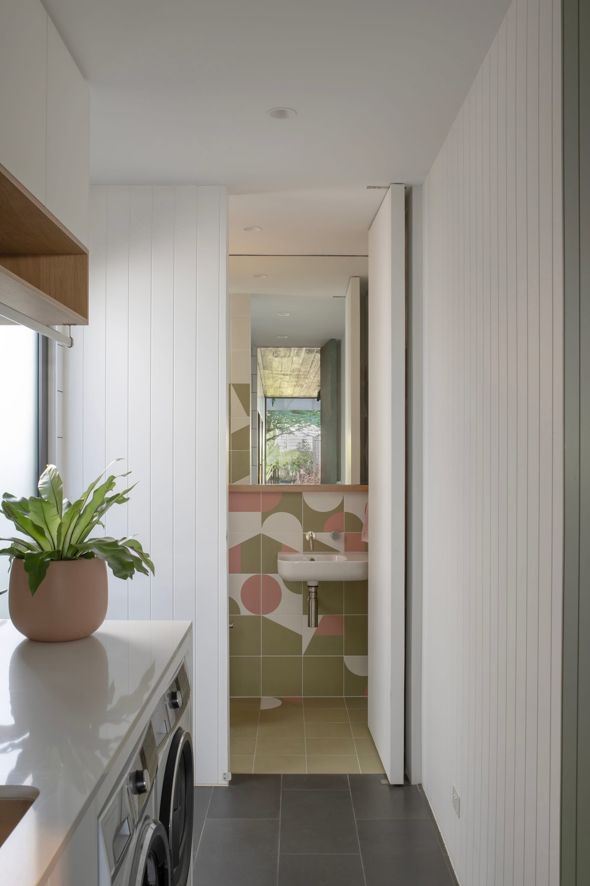 Cornerstone by Loupe Architecture. Photography by Alanna Jayne McTiernan. Ensuite with patterned sage and pink splash back tiles and floor tiles, coming off hallway with white clad timber walls. 